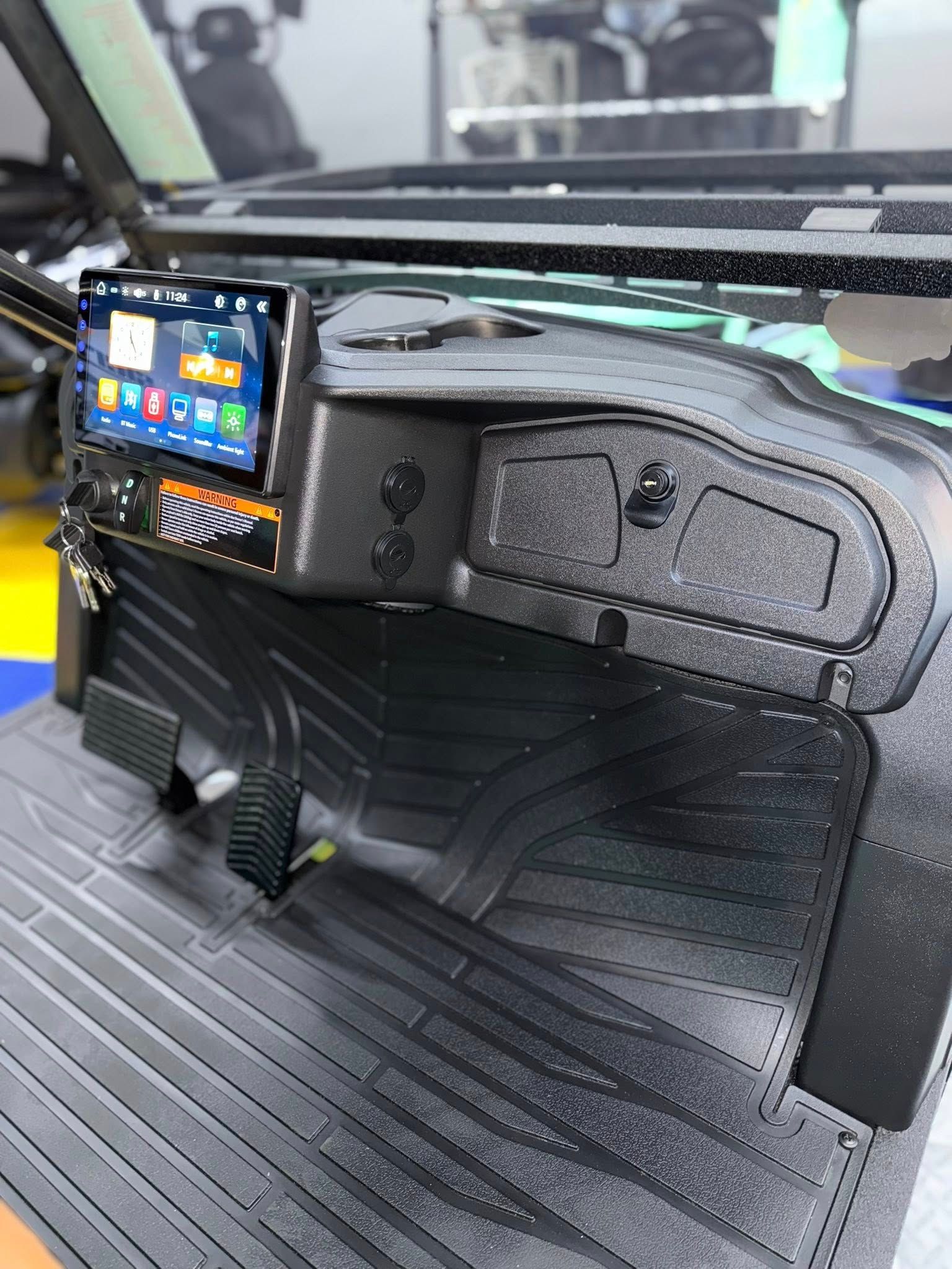 Black golf cart dashboard with mounted screen, controls, and textured floor mat.