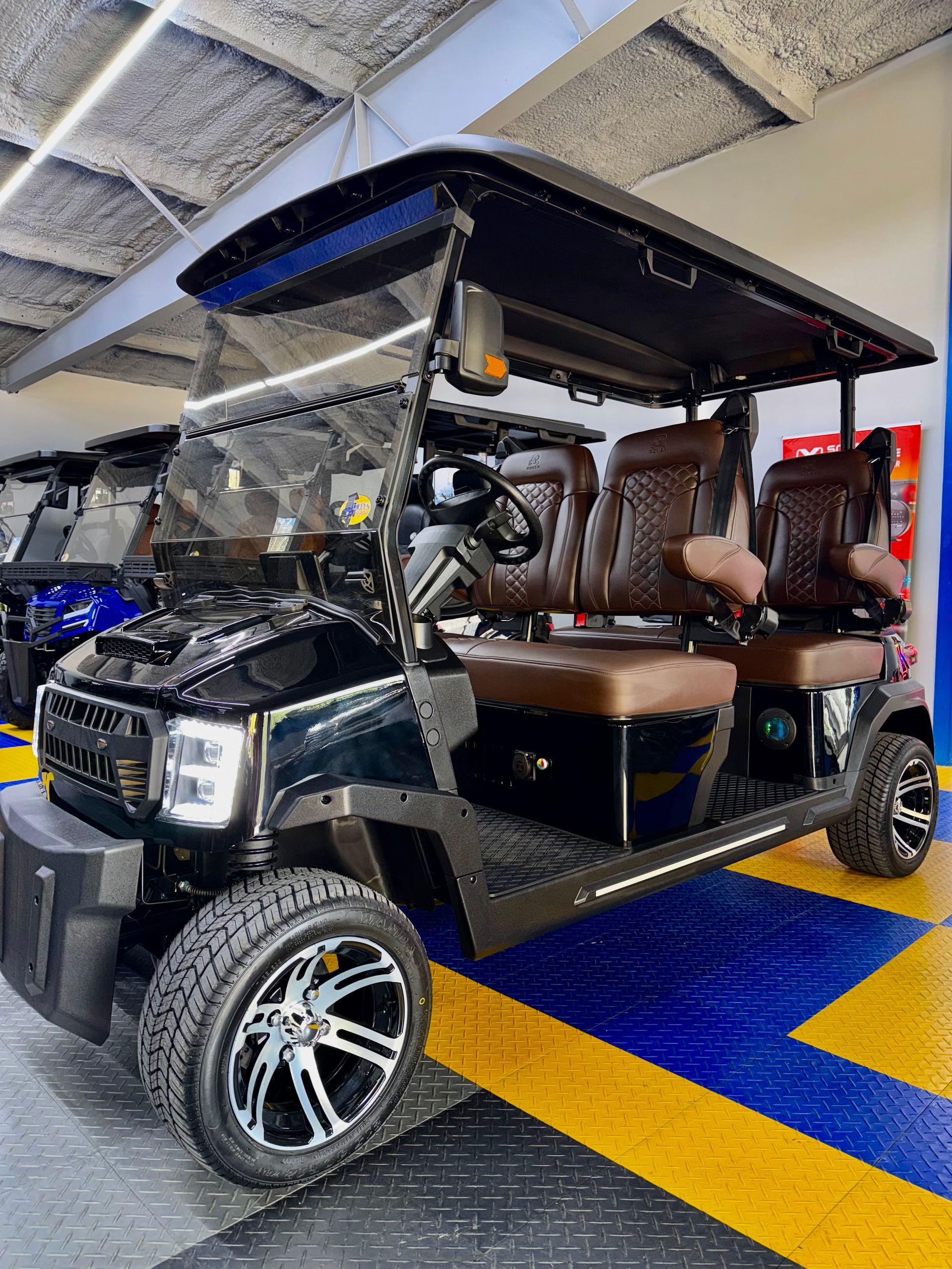 Black golf cart with tan seats parked indoors on a blue and yellow floor.