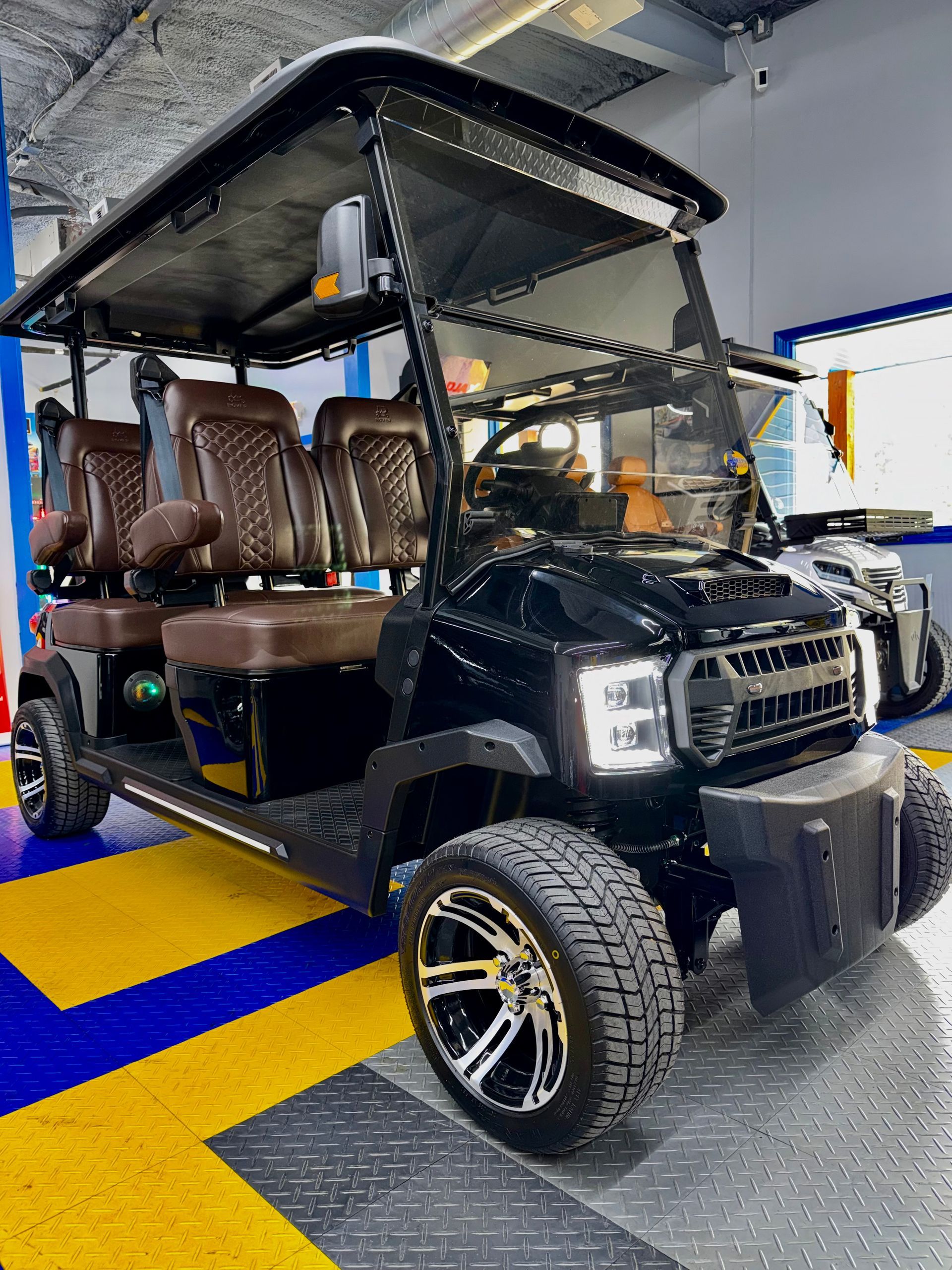 Black golf cart with tan seats and a canopy, parked indoors on a showroom floor.