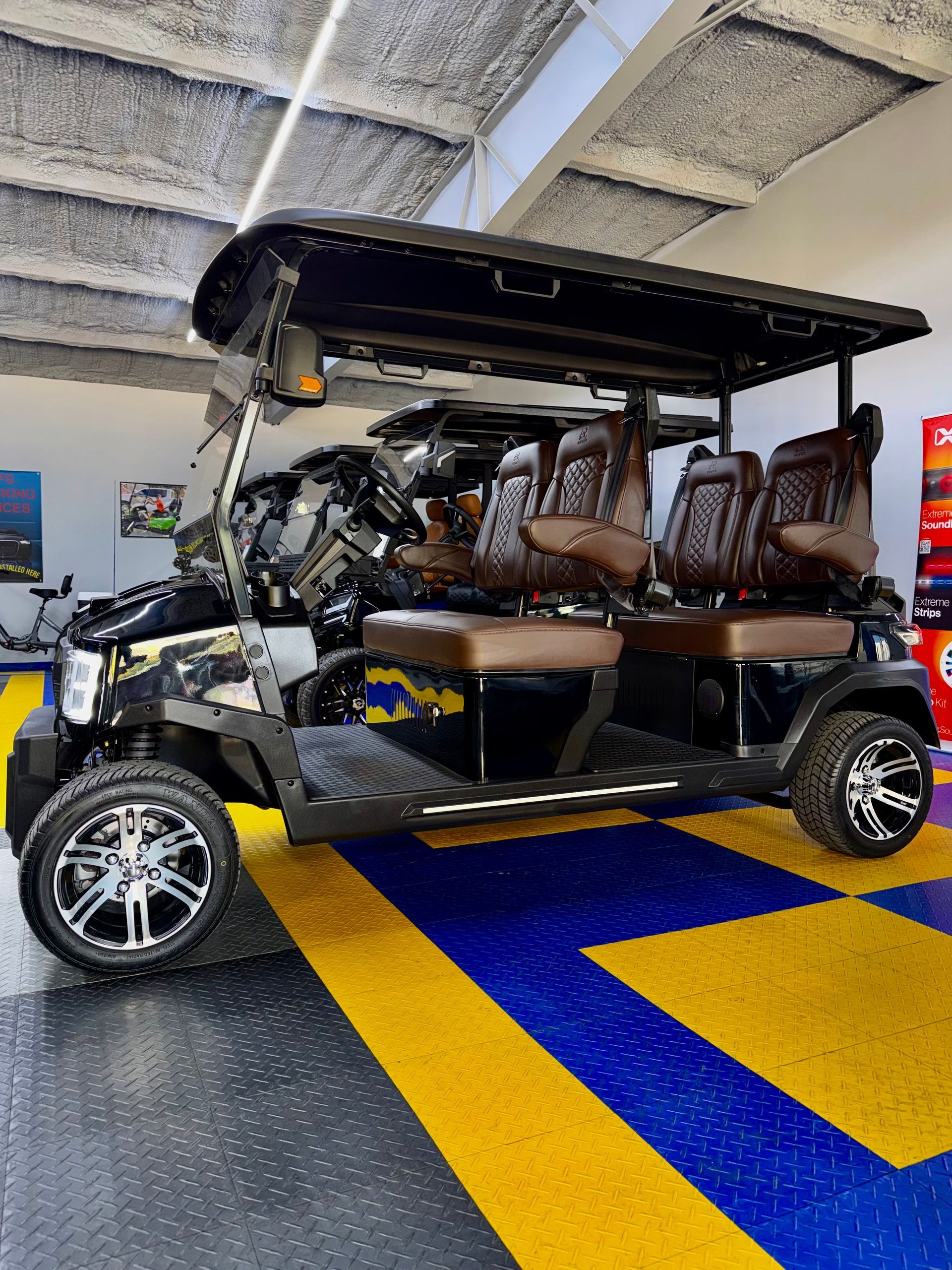 Black golf cart with tan seats and black canopy parked indoors on blue and yellow floor stripes