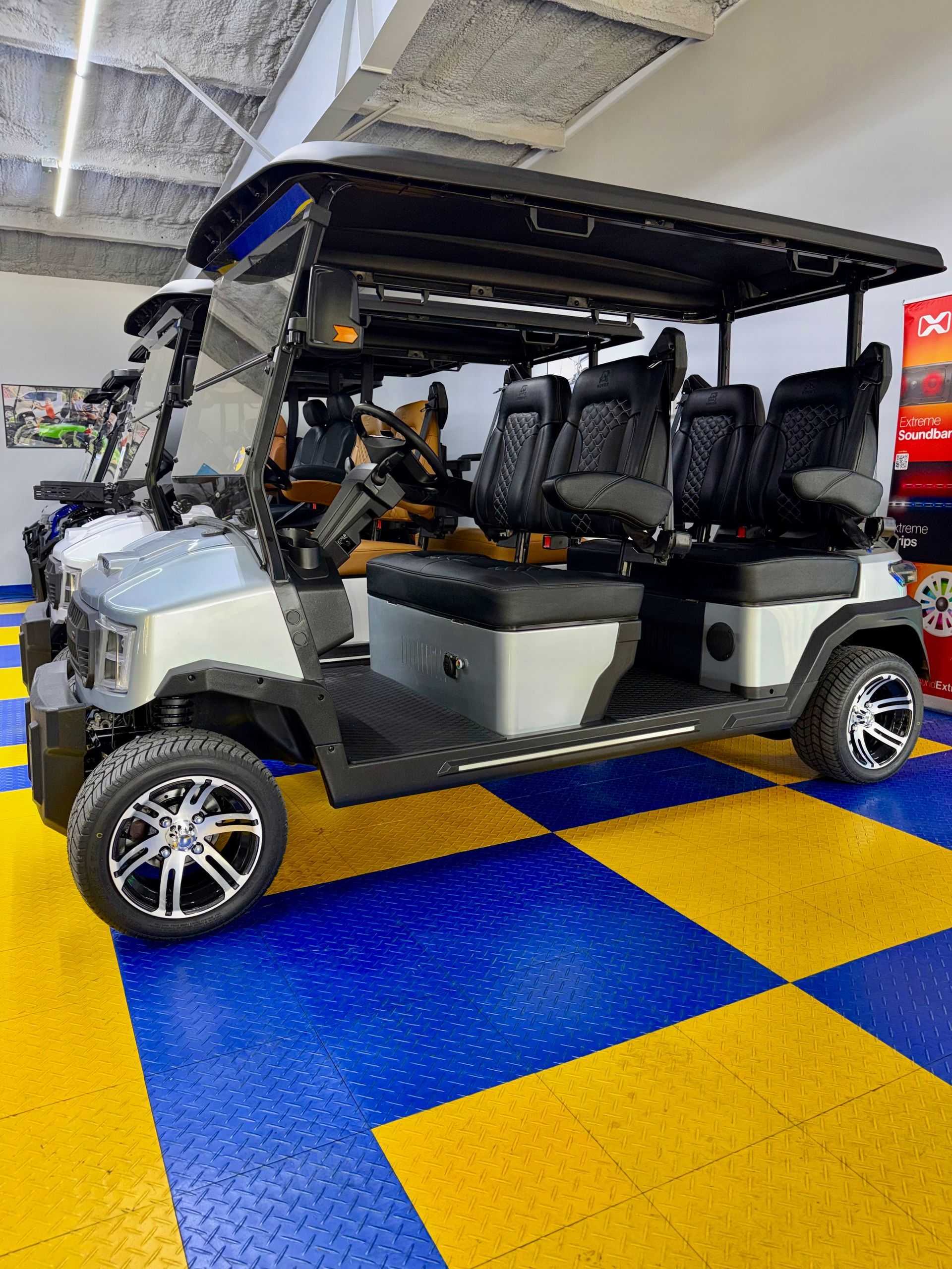 White golf cart with black roof and seats parked on a blue-and-yellow checkered floor indoors