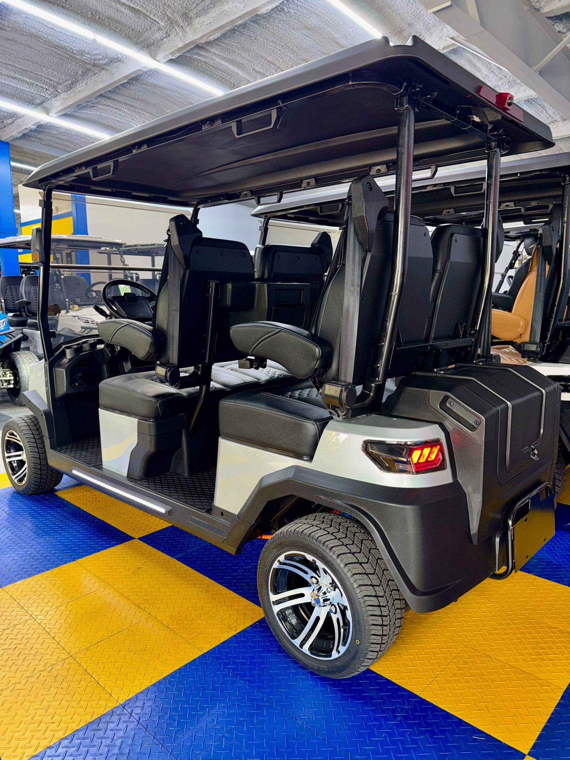 Black golf cart with open sides and roof displayed indoors on a blue-and-yellow checkered floor.