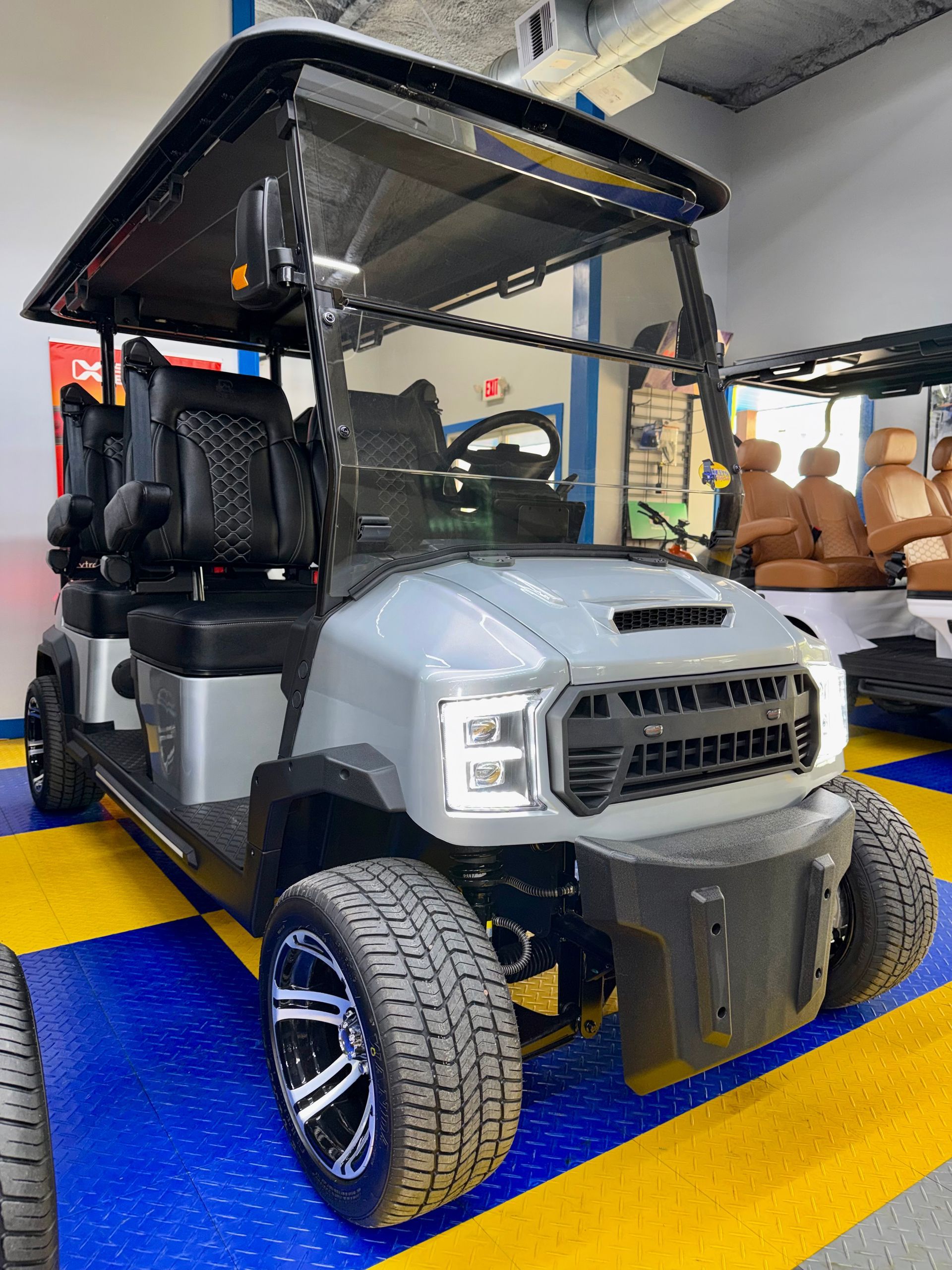 Gray golf cart with roof and black seats on a blue mat in a workshop