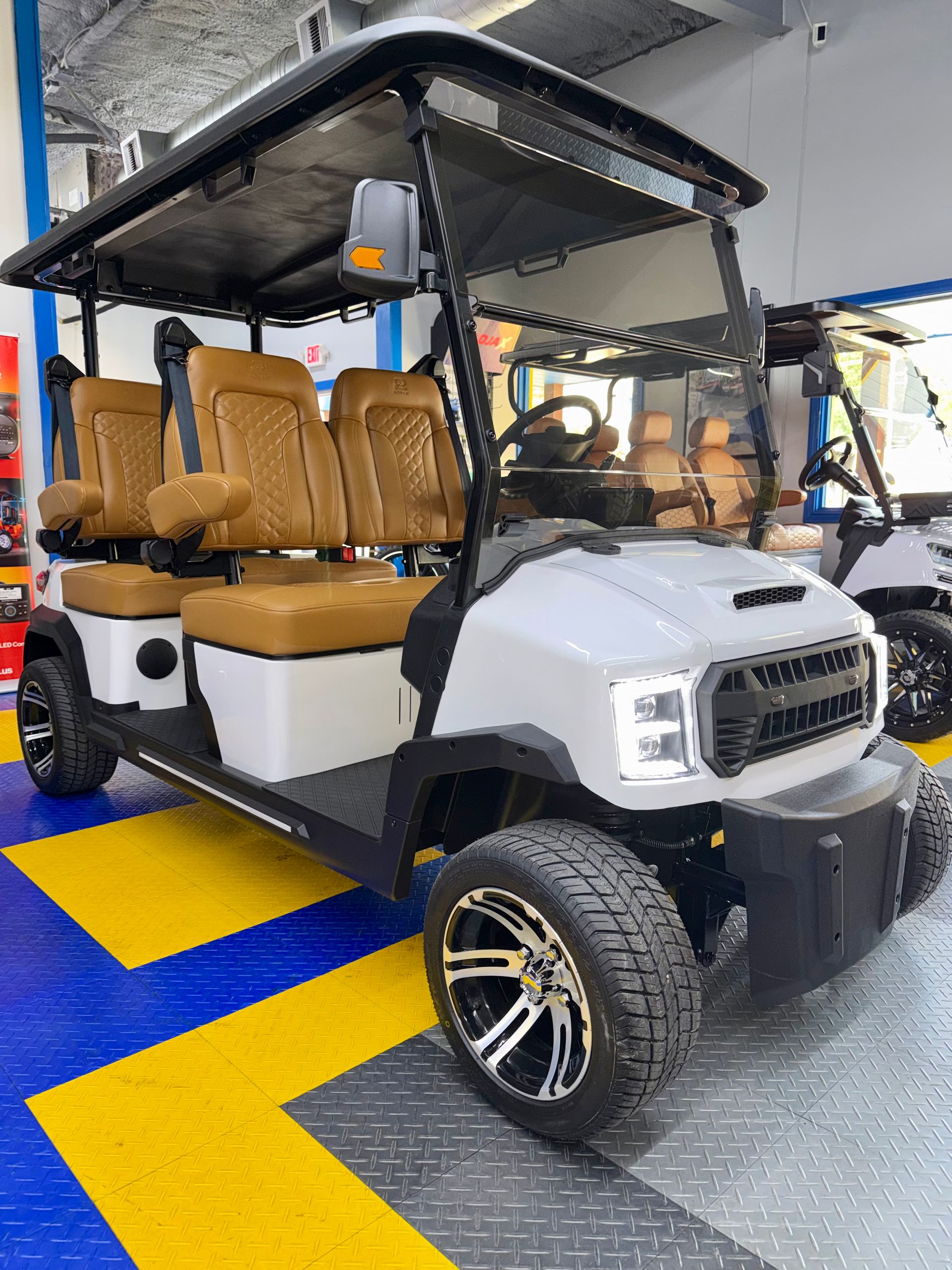 White golf cart with tan seats and large wheels parked indoors on a blue and yellow floor.