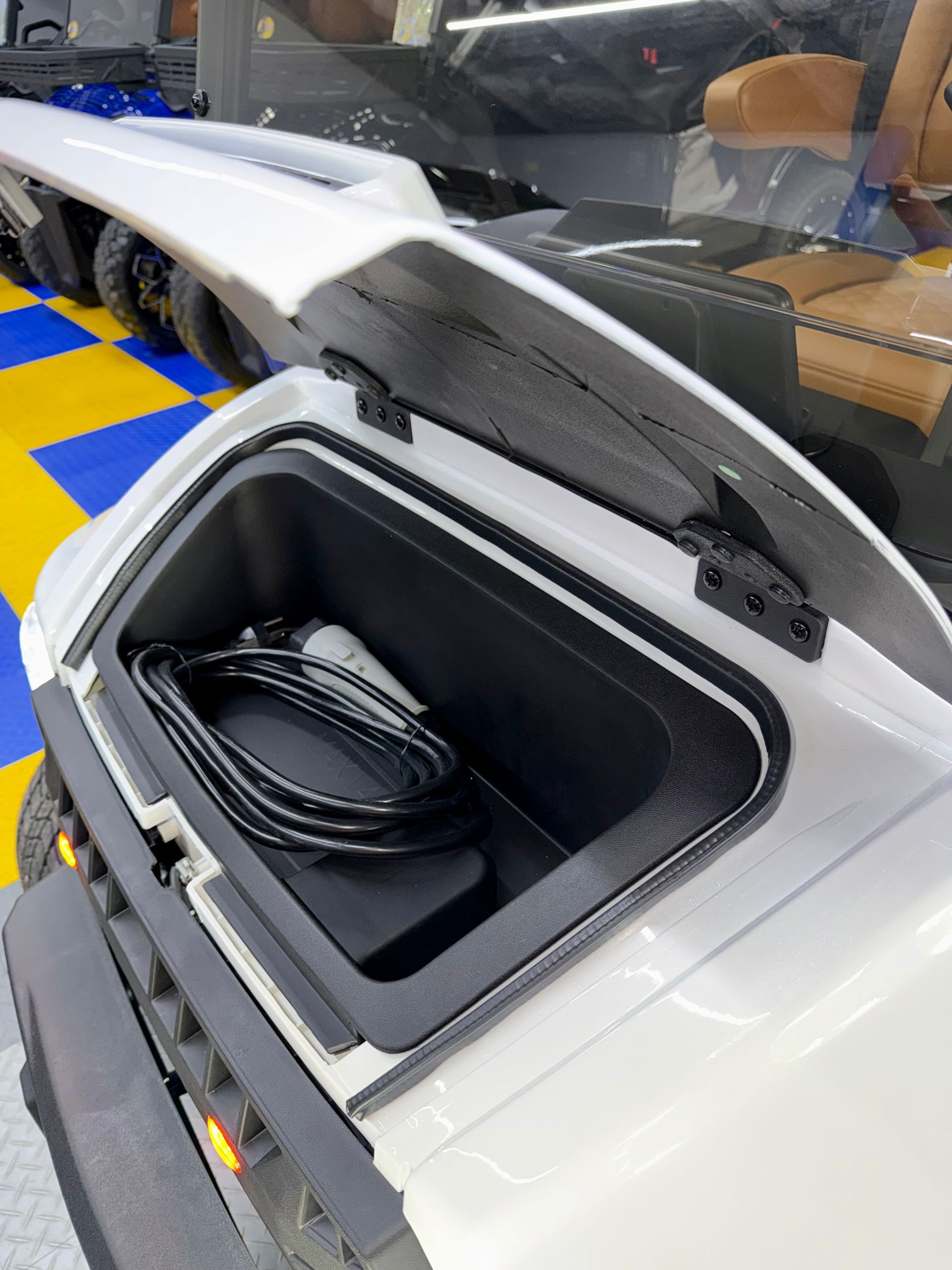 Open vehicle storage compartment with coiled cable inside, white car body and black-lined trunk opening