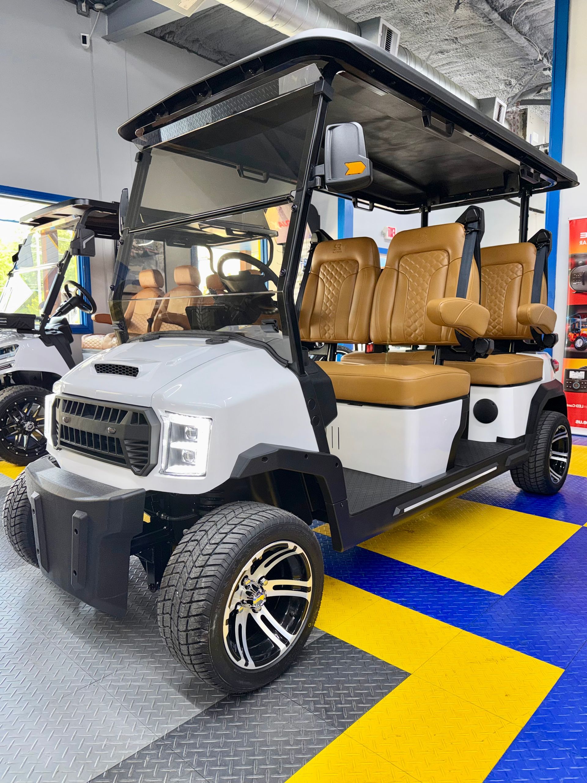 White utility golf cart with tan seats parked indoors on a blue and yellow floor.