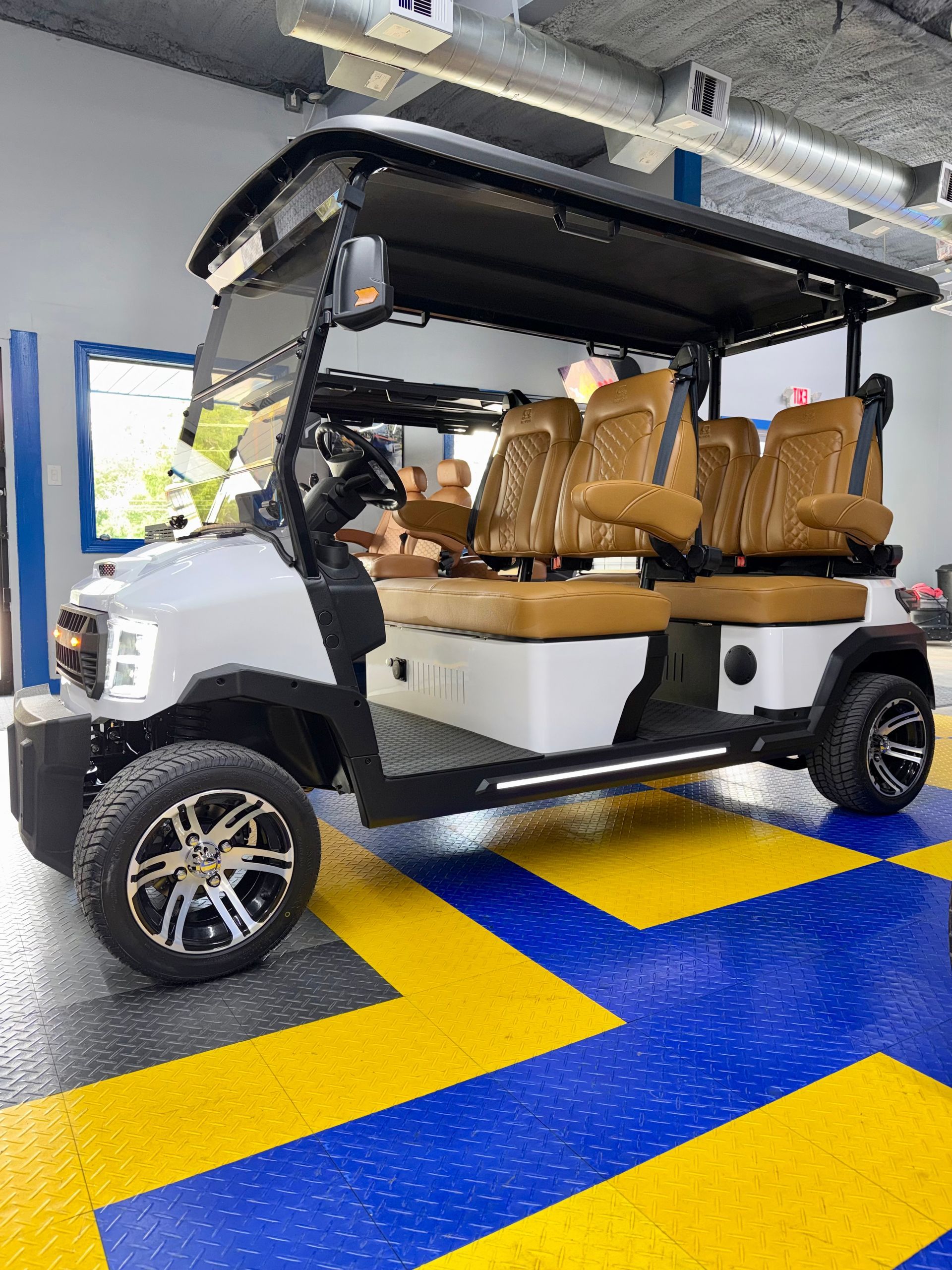 White utility cart with tan seats parked indoors on a blue and yellow floor.
