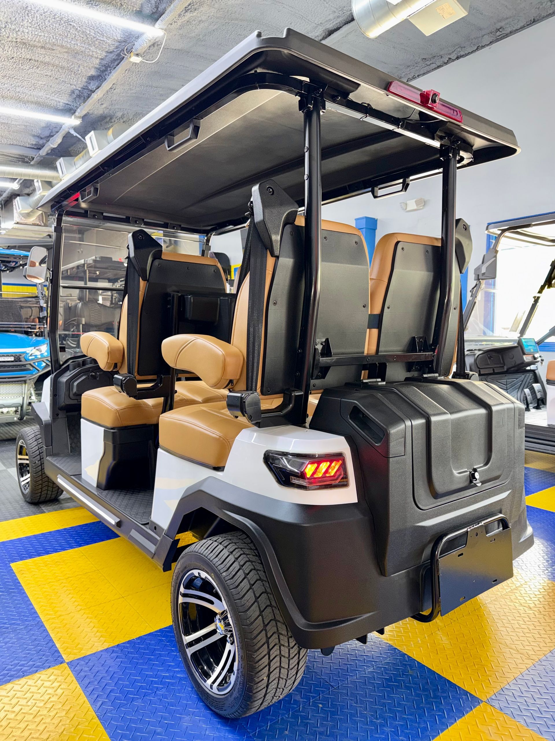 Black golf cart with tan seats in an indoor showroom, viewed from the rear.