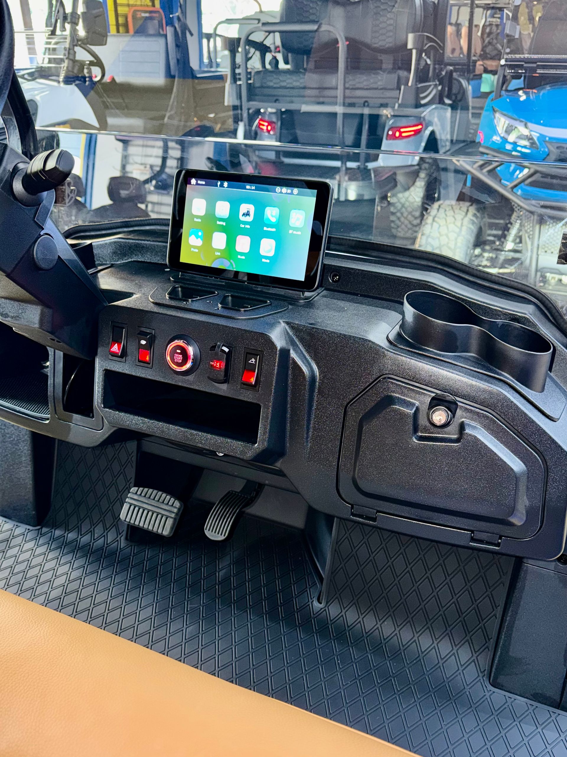 Dashboard of a vehicle with a mounted tablet, control switches, and pedals visible behind the wheel.