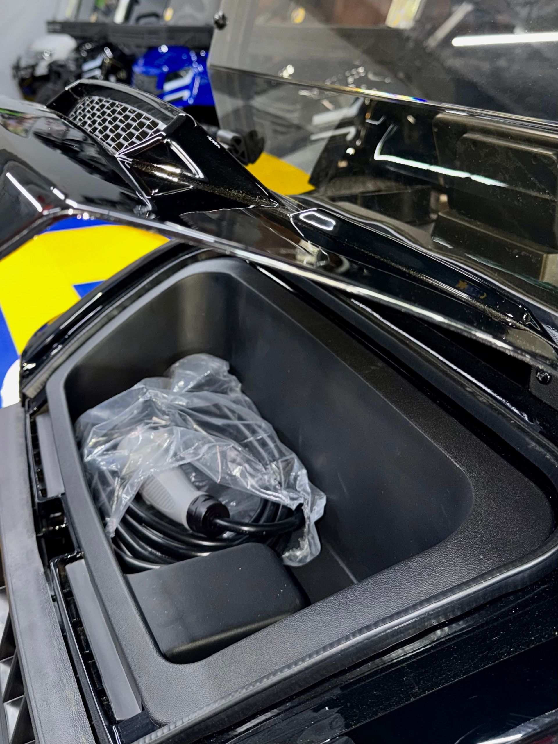 Open motorcycle storage compartment with a plastic-wrapped item inside, beside a blue and yellow fairing.