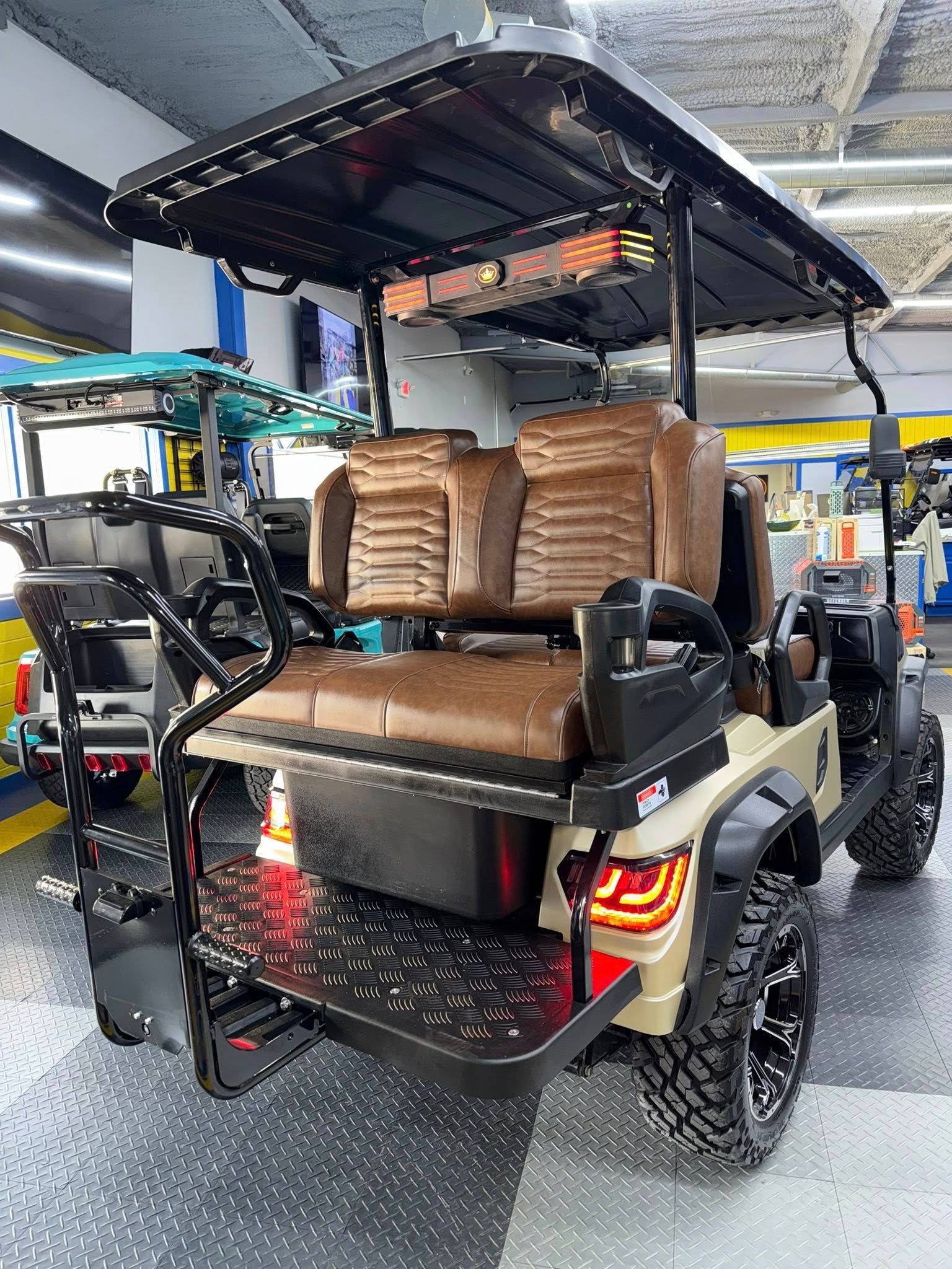 Tan golf cart with brown seats, black roof, and off-road tires. Tailgate and taillights visible.