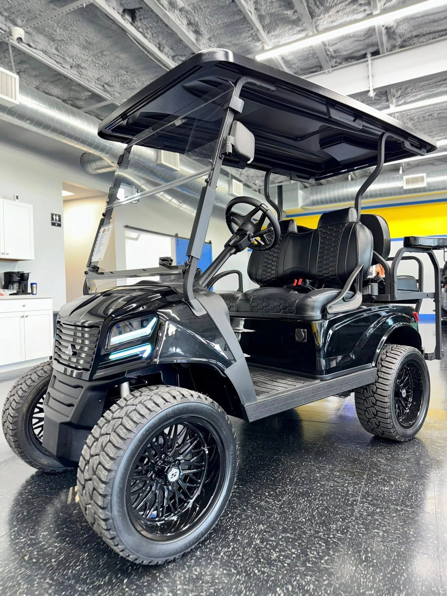 Black custom golf cart with large tires, a sun shade, and tinted windshield.