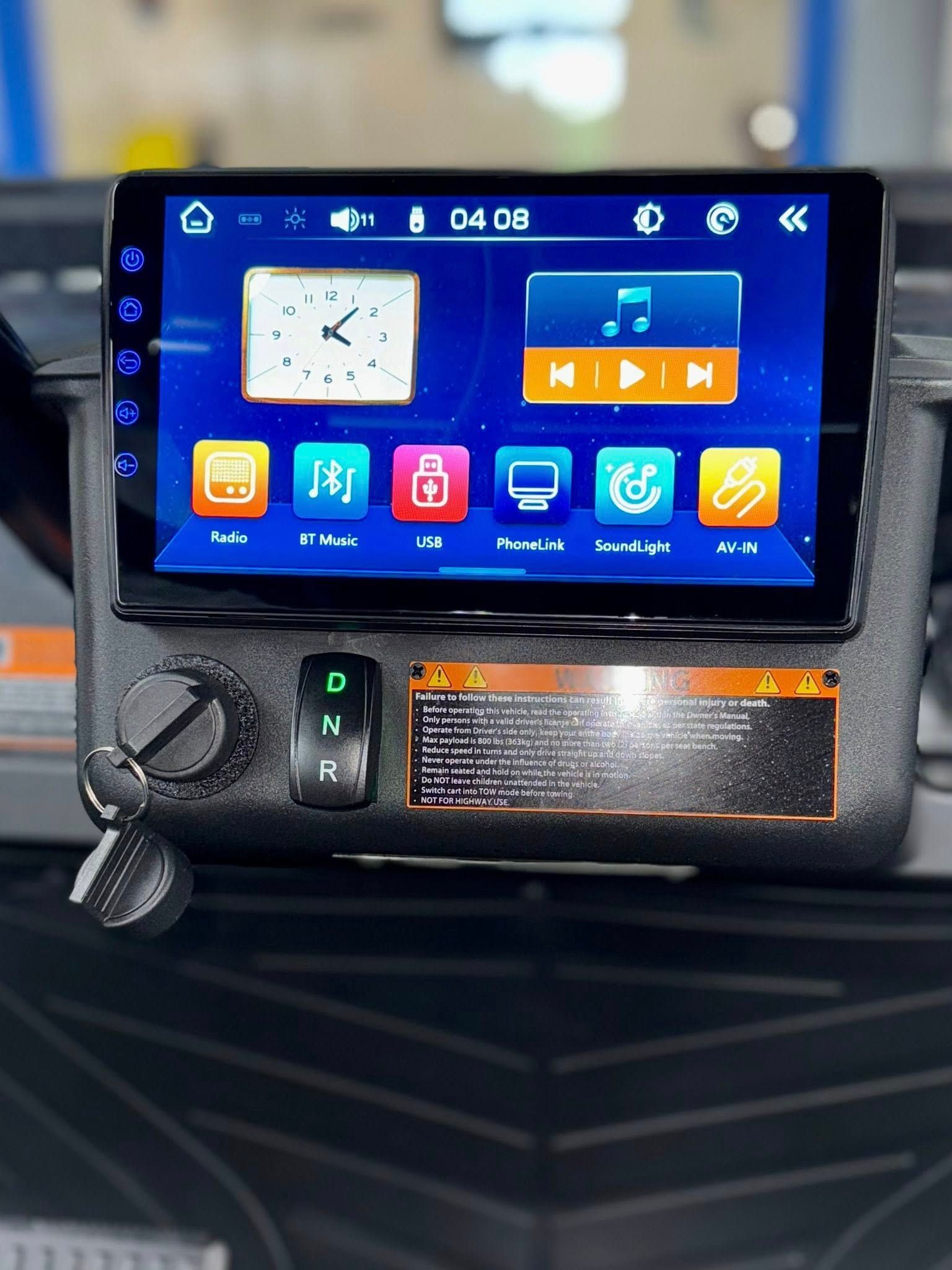 Black dashboard with a touchscreen display, clock, and music controls, plus buttons and a key.