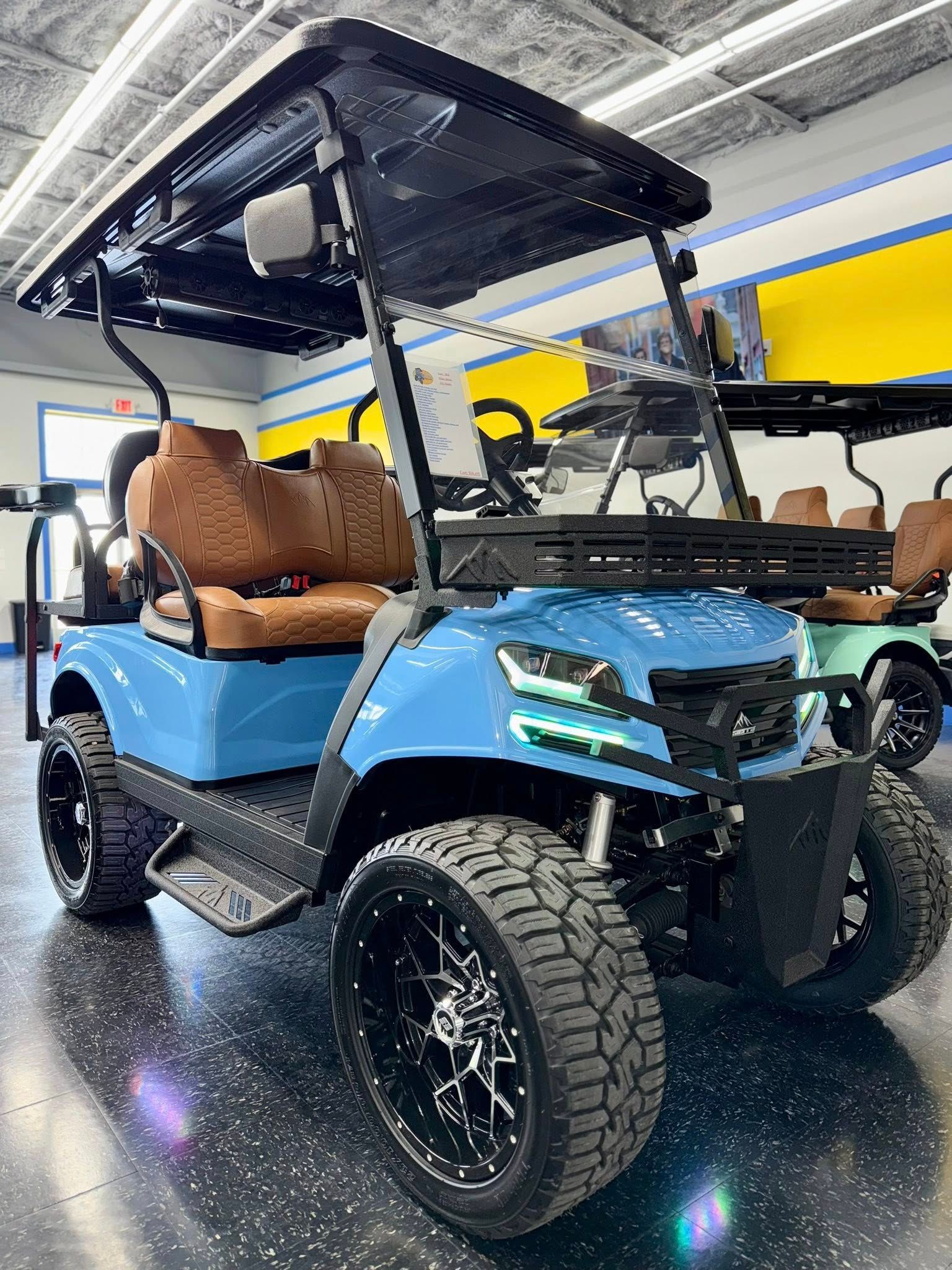 Blue golf cart with black roof, brown seats, large wheels. Inside a showroom.