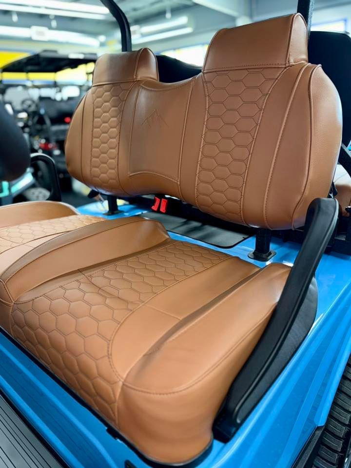 Tan leather golf cart seats with honeycomb stitching, set on a blue cart.