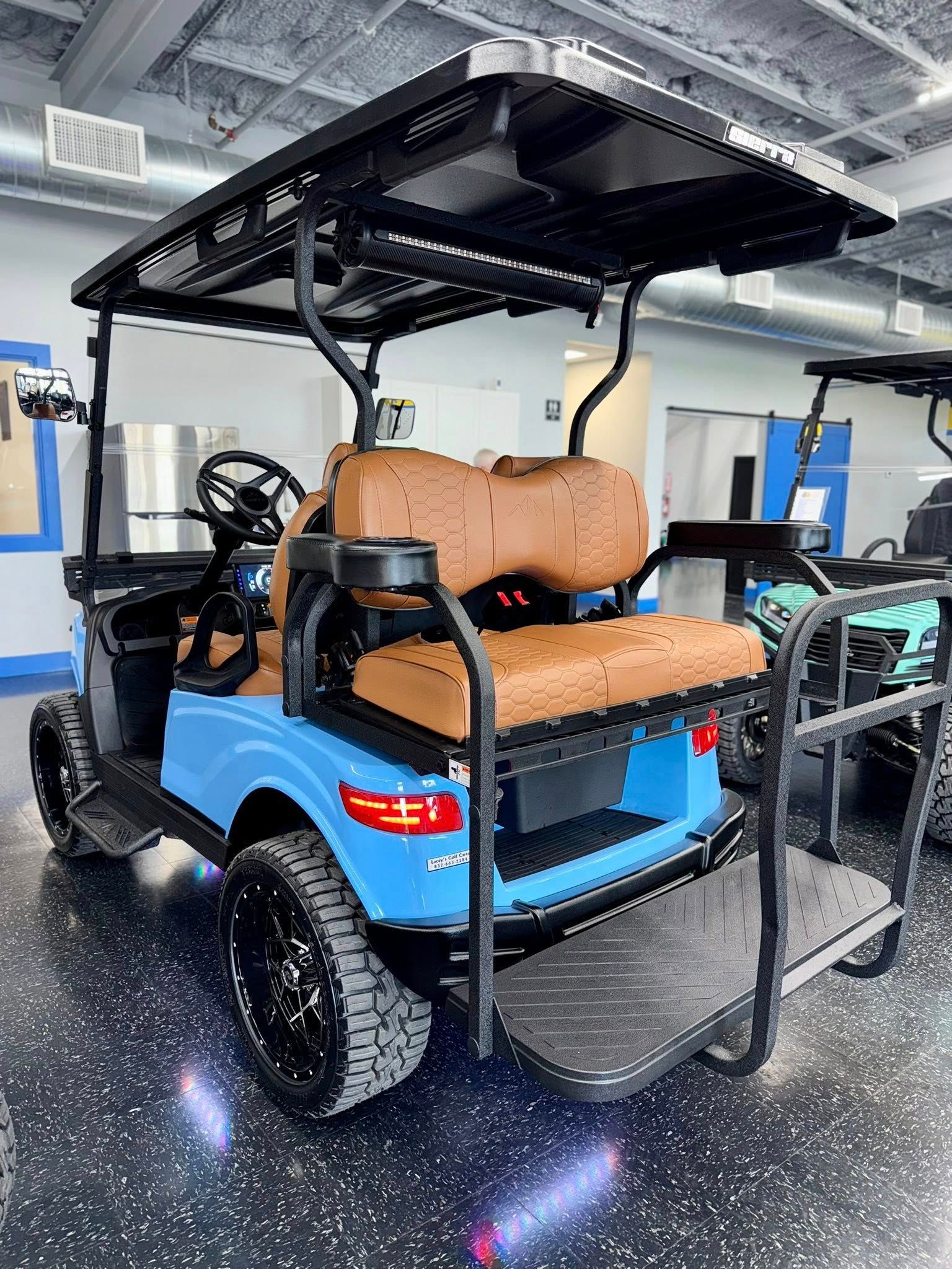 Blue golf cart with brown seats, black wheels and roof, inside a showroom.