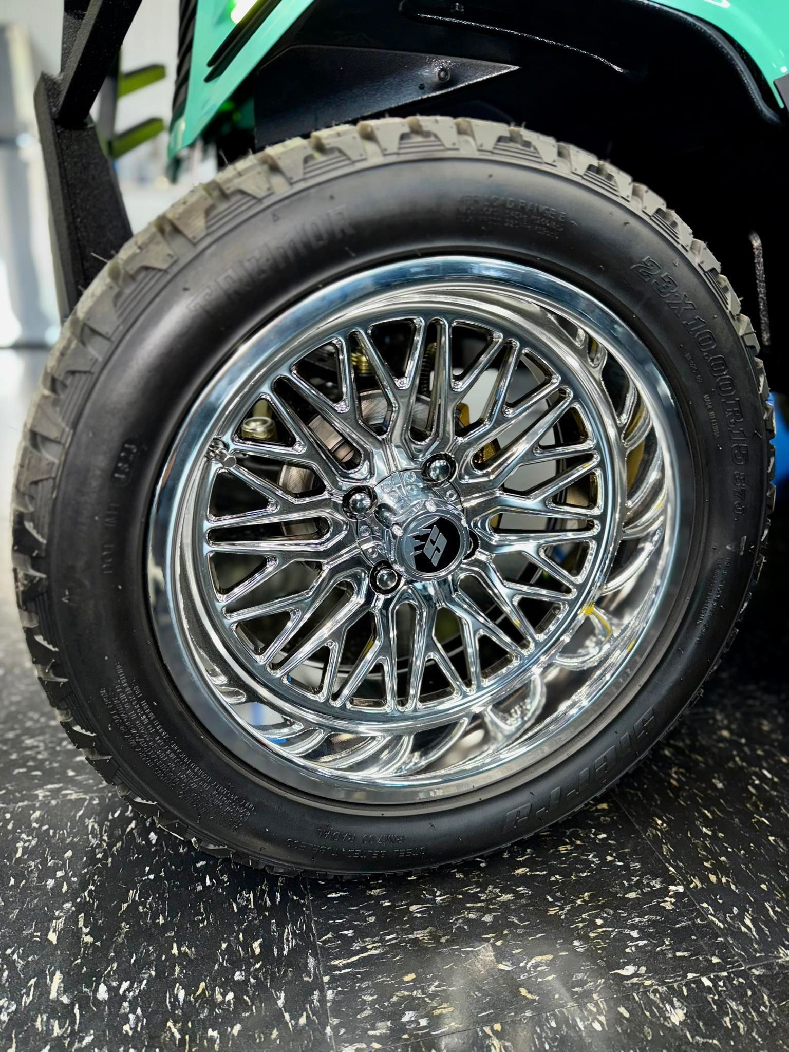 Close-up of a black tire with a chrome wire wheel on a vehicle, set indoors on a dark floor.
