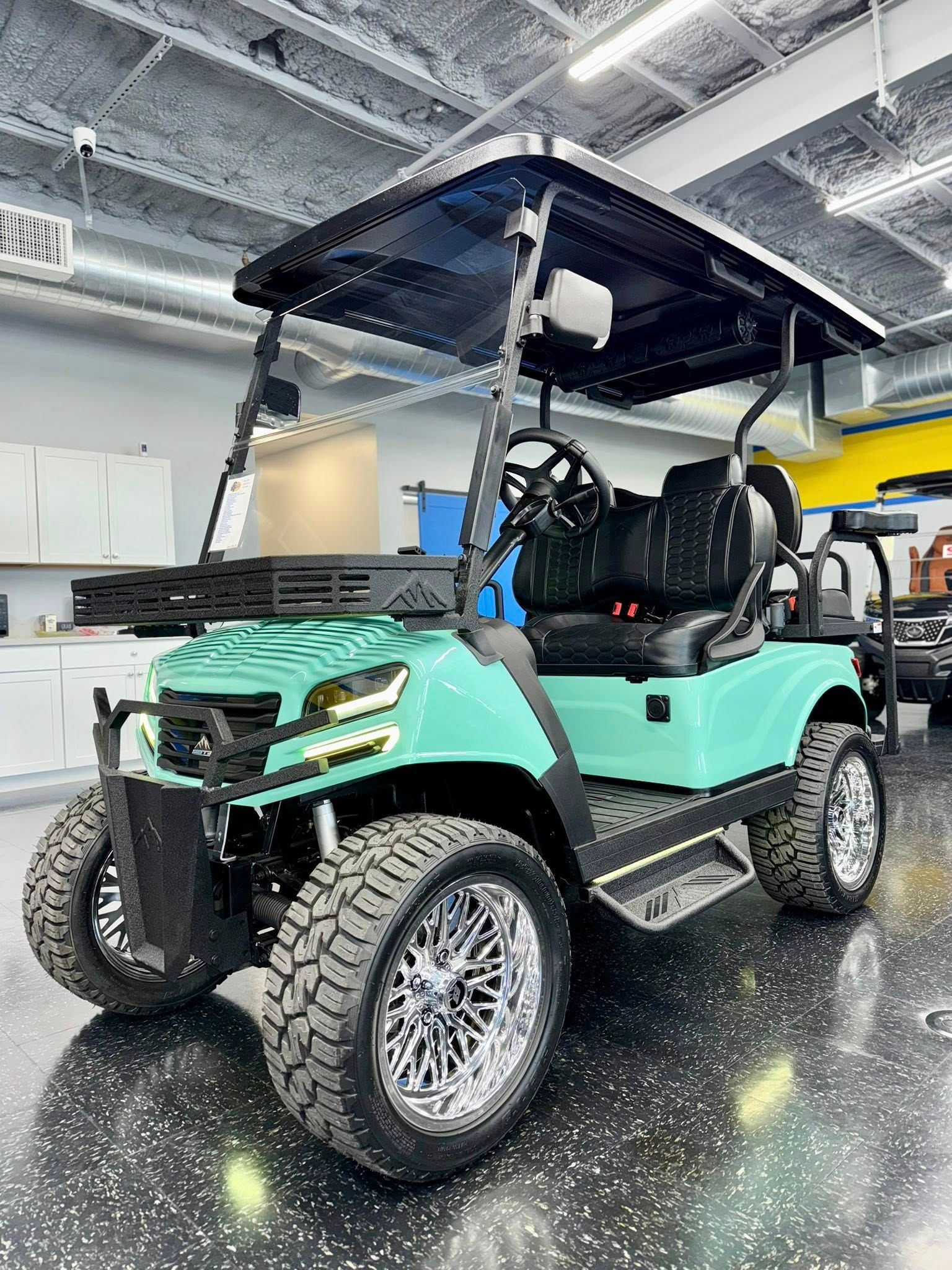 Aqua golf cart with black roof, large wheels, chrome rims, inside a garage.