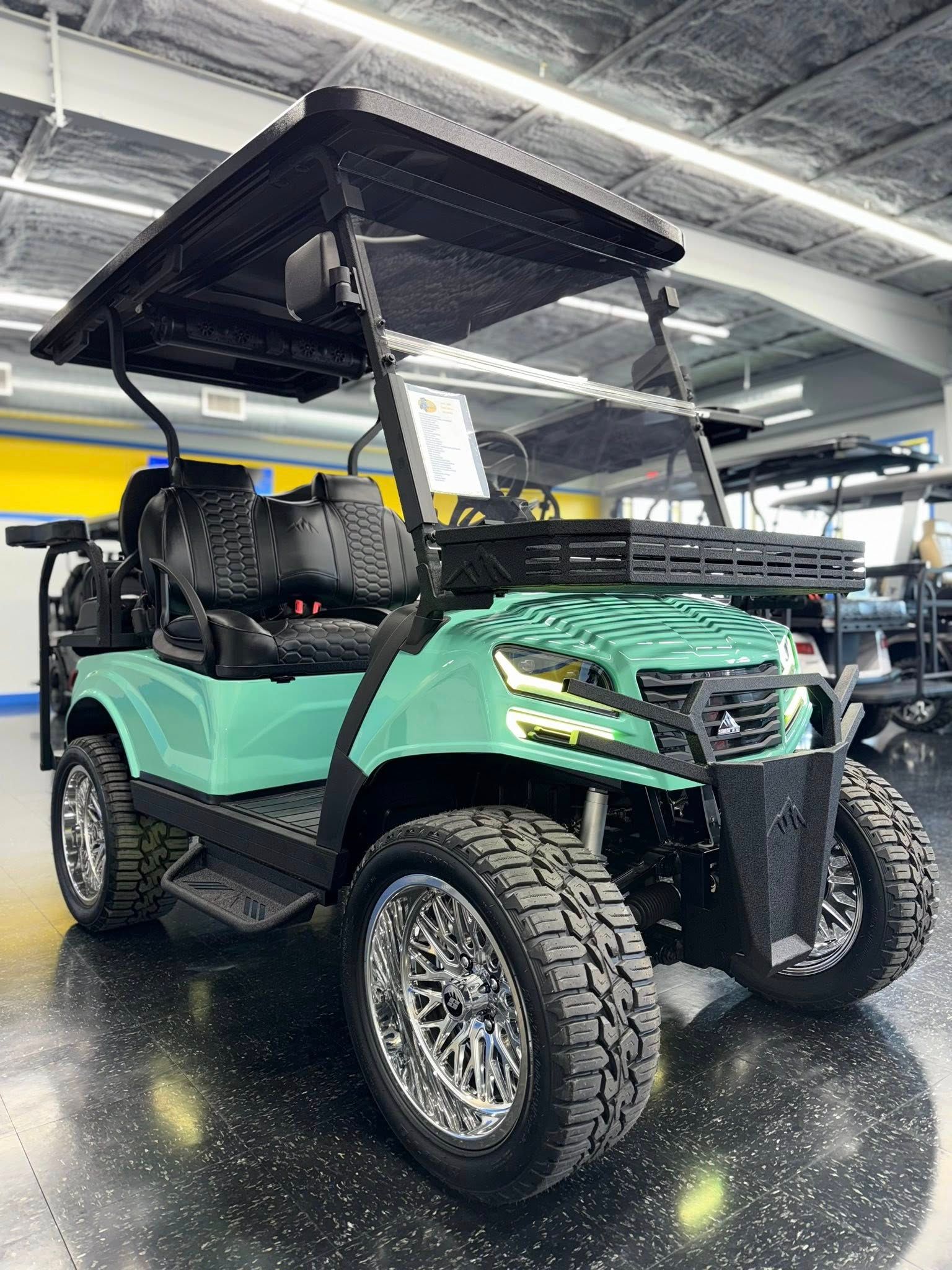 Mint green golf cart with black roof, chrome wheels, and off-road tires inside a showroom.