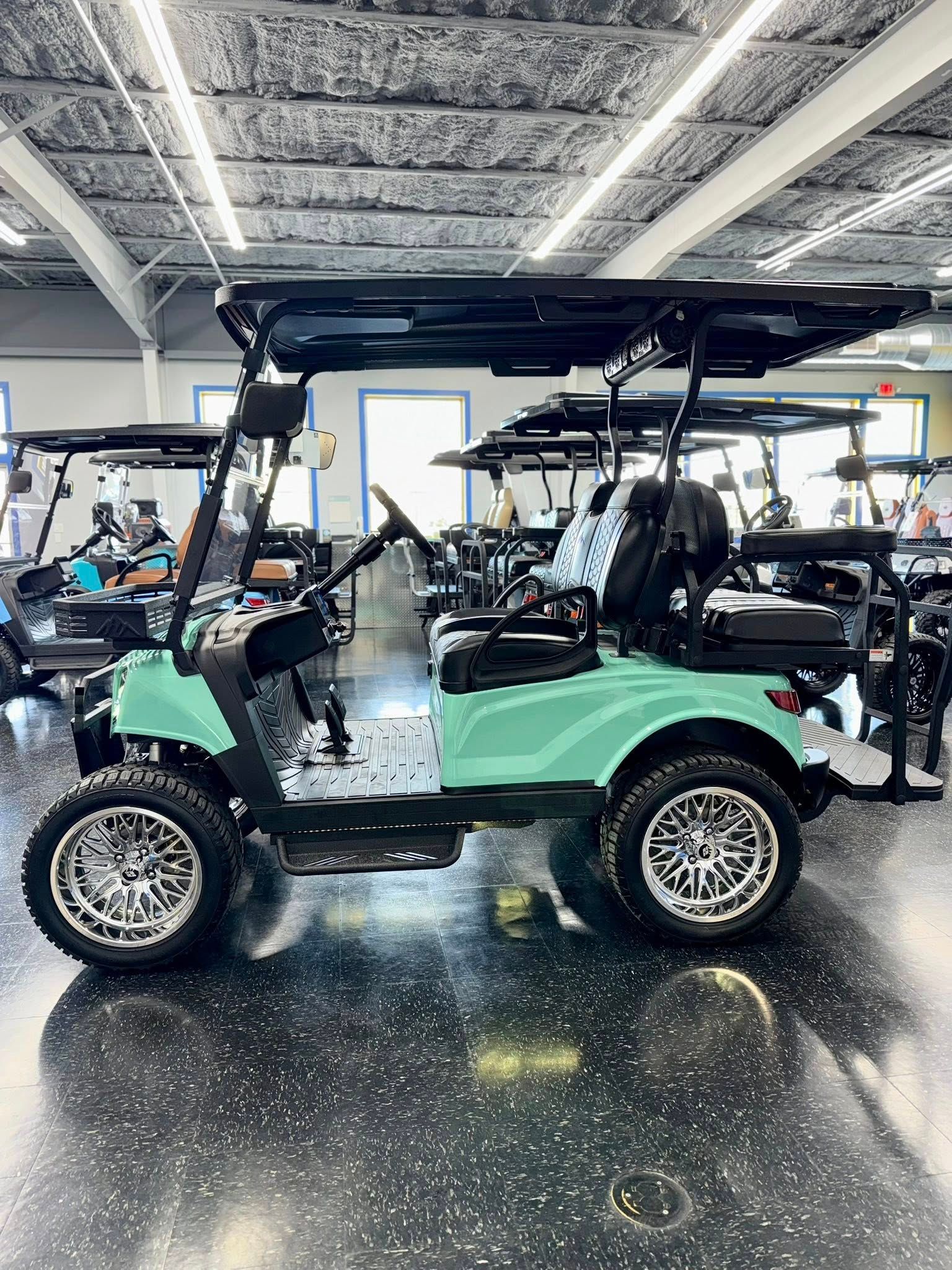 Teal golf cart with black roof and chrome wheels parked in a showroom.