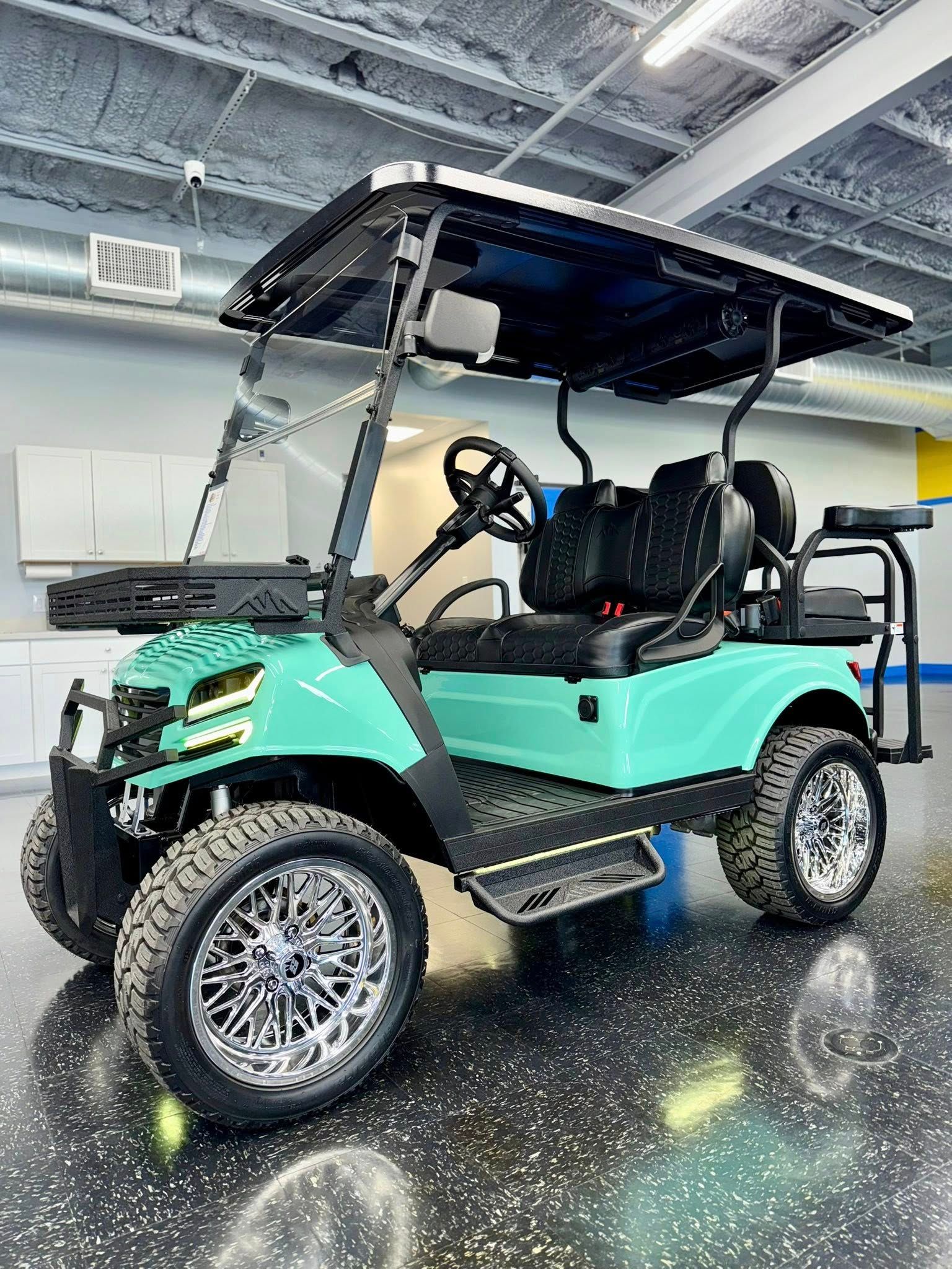 Teal golf cart with black roof, large chrome wheels, and black seats, in a showroom.