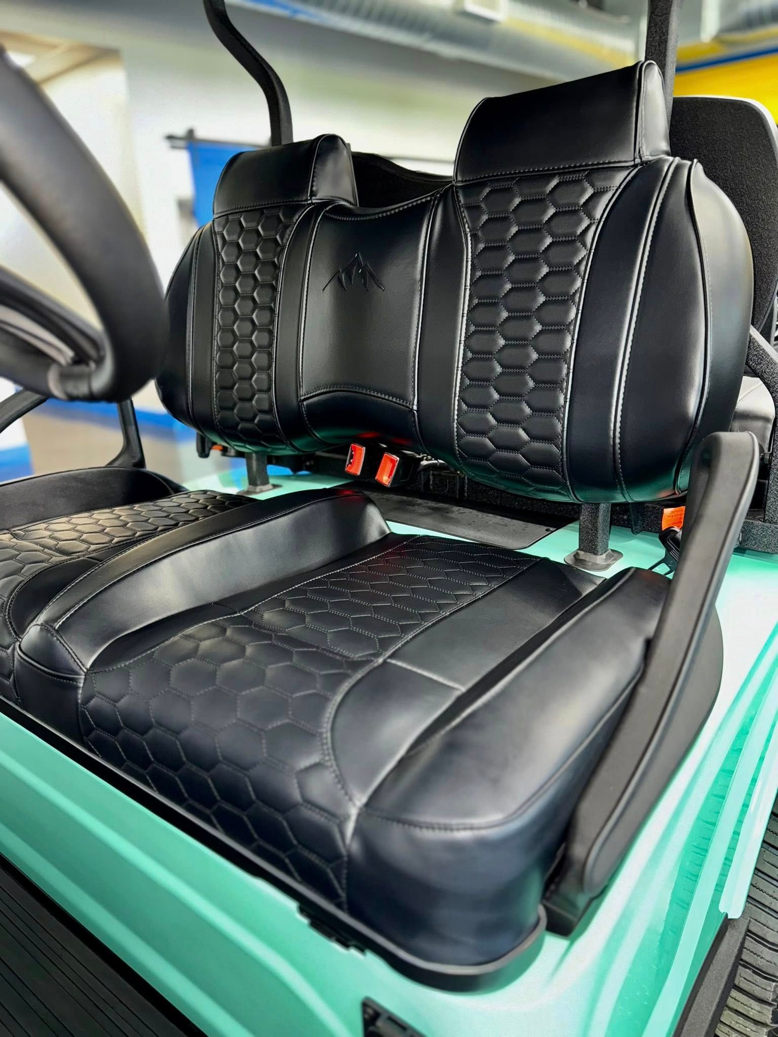 Black golf cart seat with honeycomb pattern and white stitching, in a turquoise cart interior.