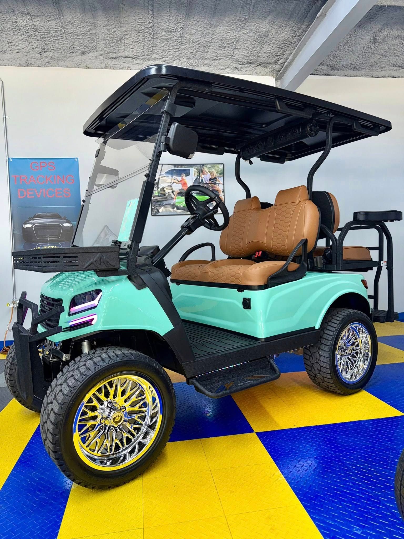 Aqua golf cart with brown seats, black roof, yellow & silver wheels on a checkered floor.