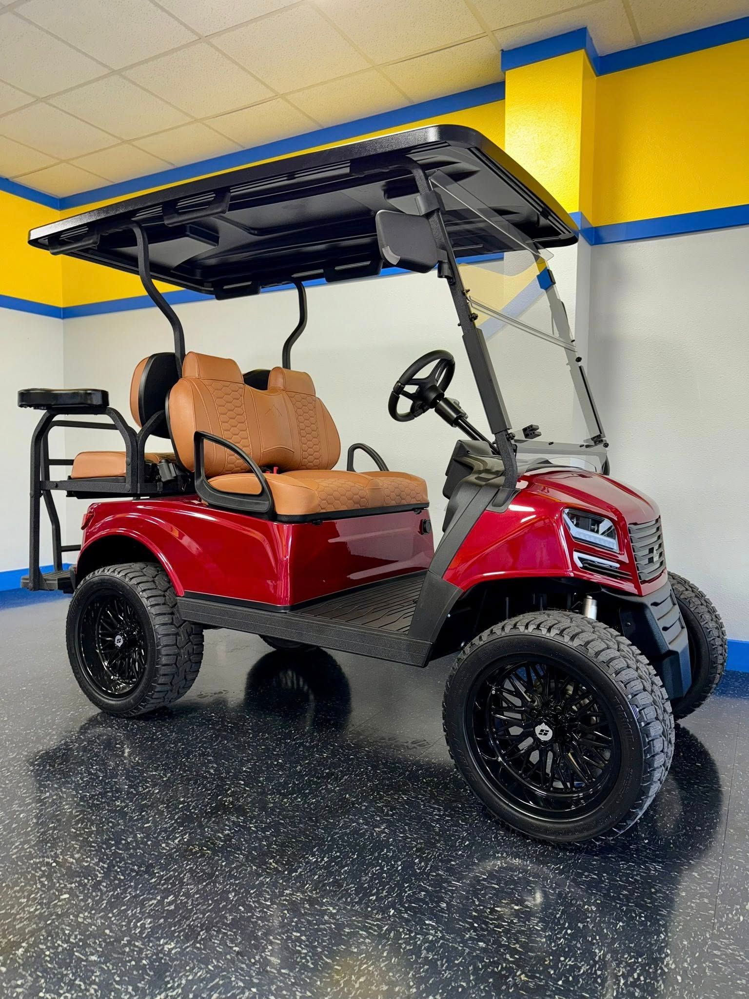Red golf cart with black wheels and roof, parked indoors with blue/yellow walls.