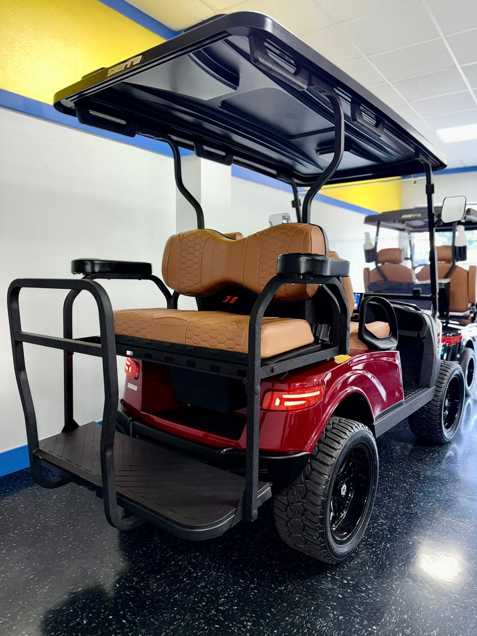 Red golf cart with black roof and wheels, brown seats, parked indoors.