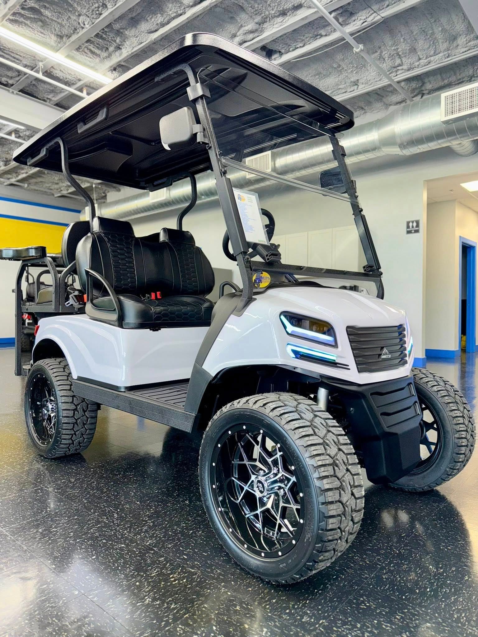 White custom golf cart with black accents, large off-road tires, and black roof, indoors.