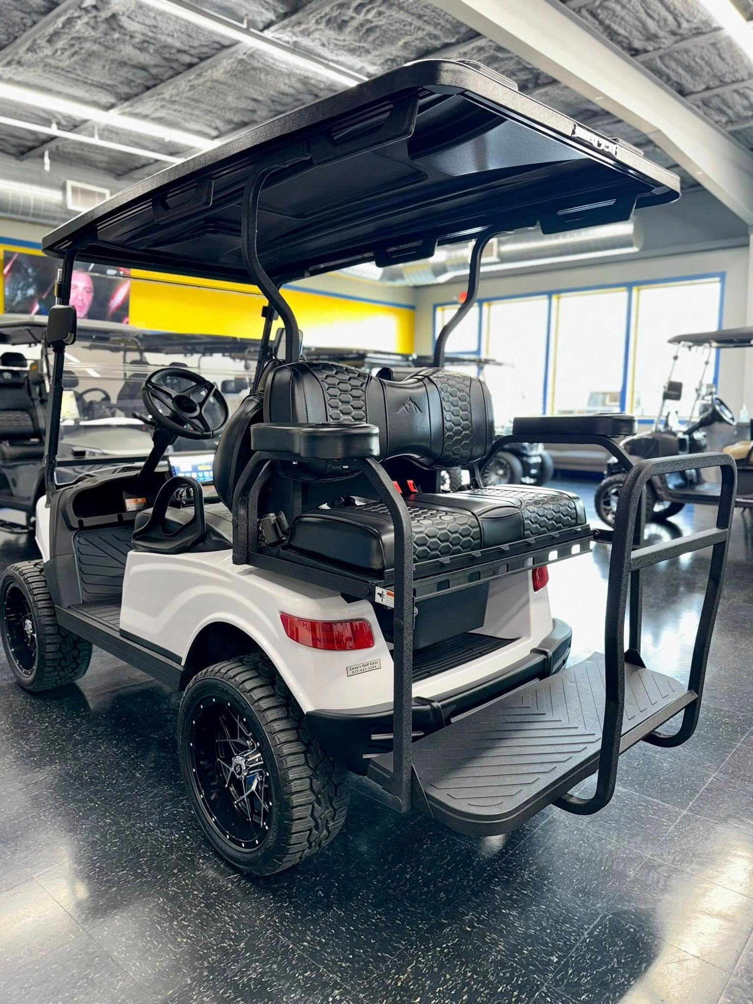 White and black golf cart with lift kit and accessories parked indoors.