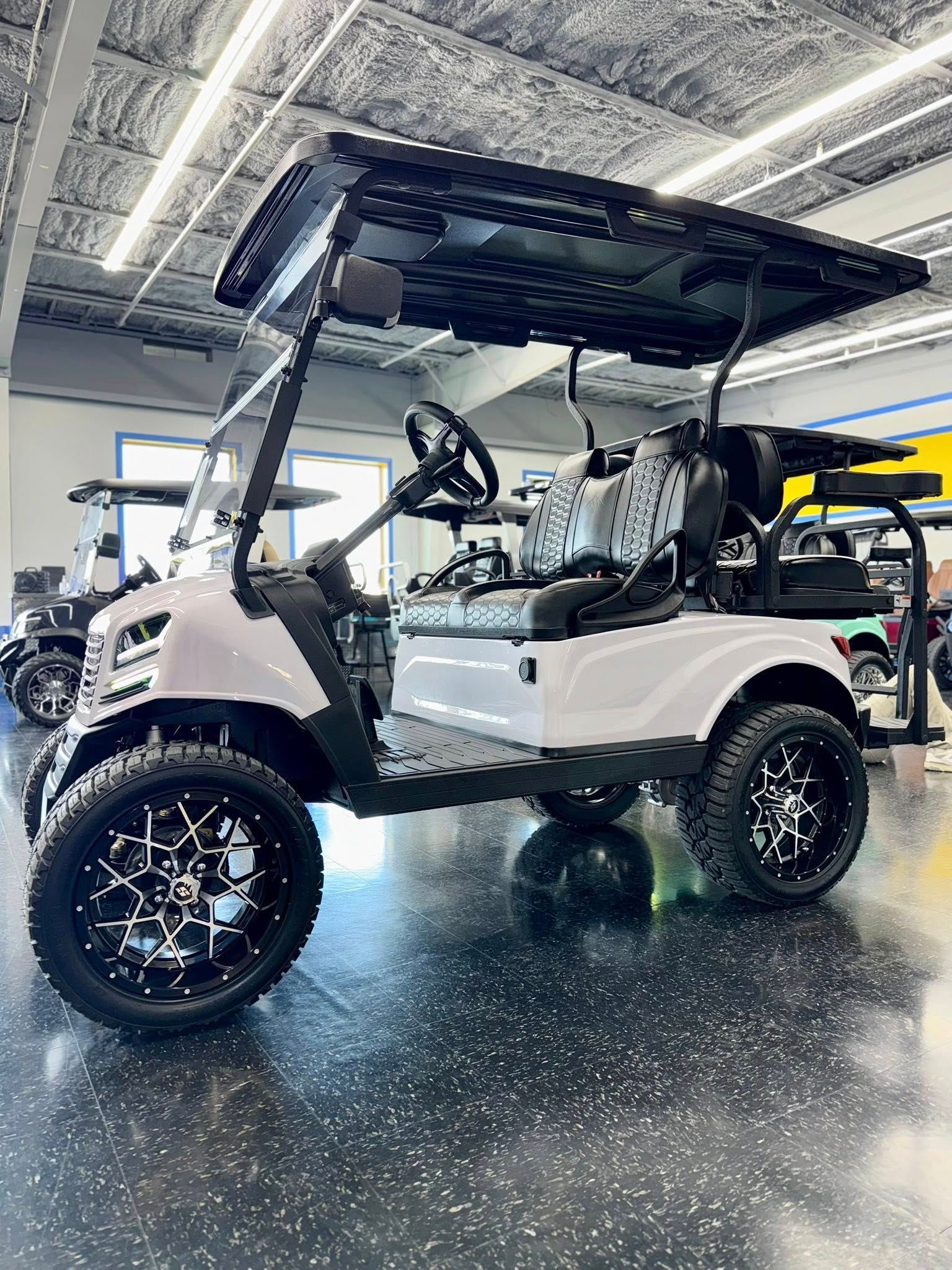 White golf cart with black accents and custom wheels, parked inside a showroom.