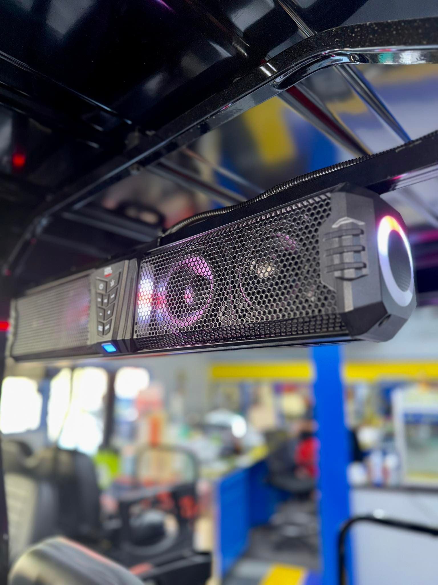 Black soundbar with lights mounted to the ceiling of a vehicle, with an out-of-focus interior background.