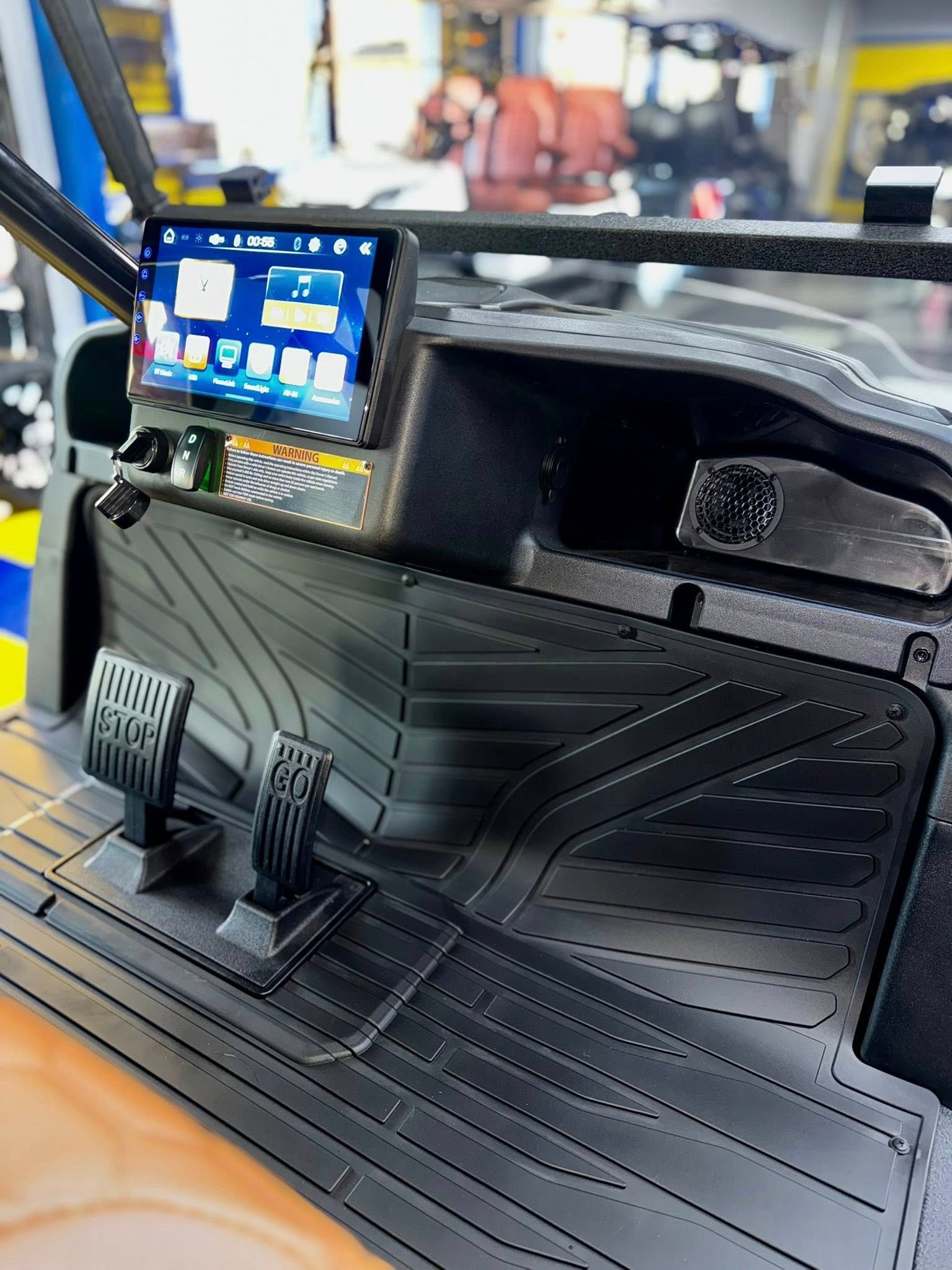 Black golf cart dashboard with a touchscreen, pedals, and textured flooring.