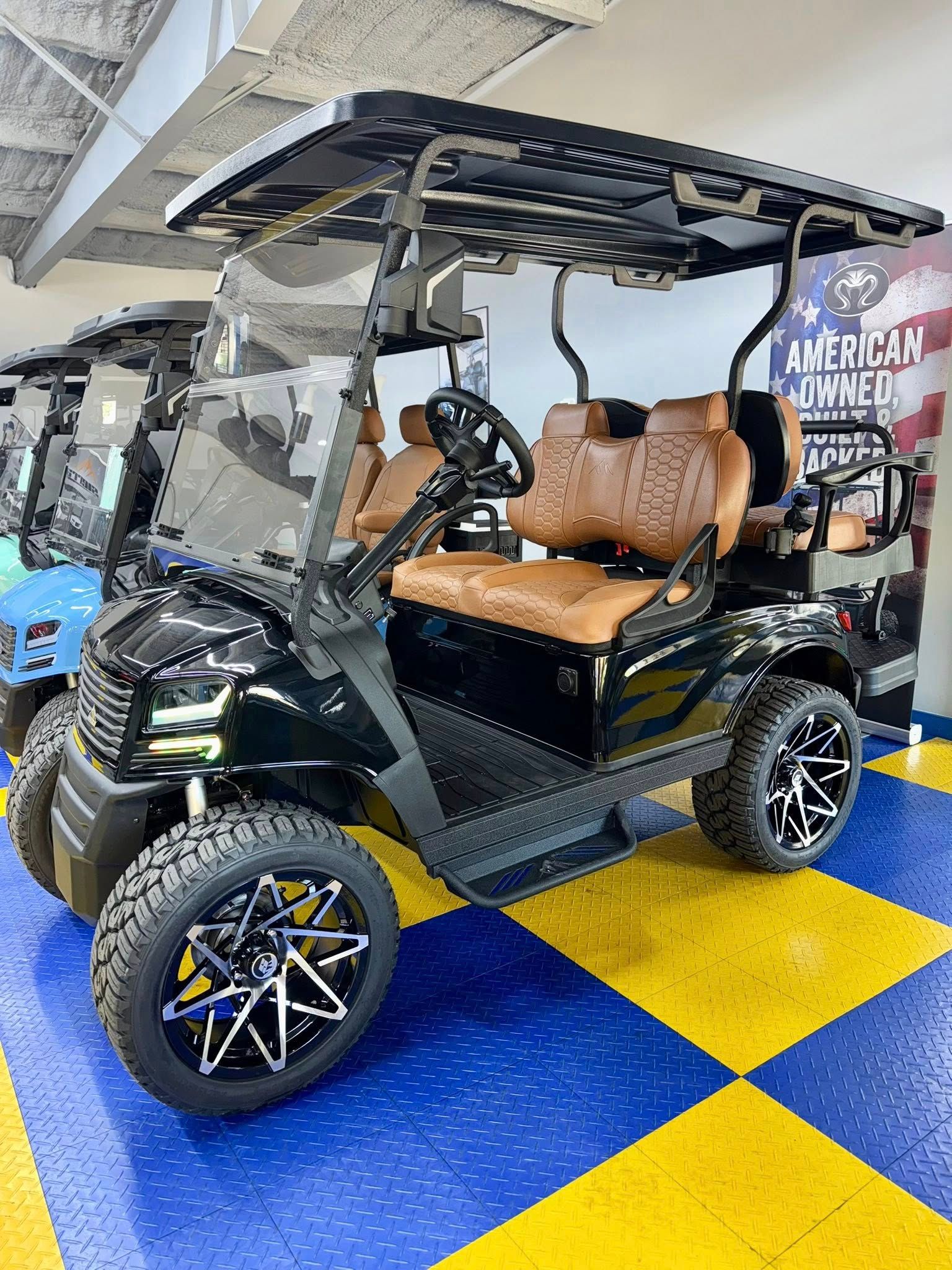 Black golf cart with brown seats, black roof, and custom wheels parked indoors.