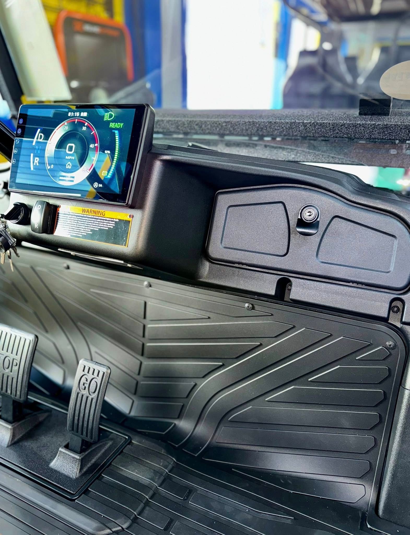 Golf cart interior with a digital dashboard, storage compartment, and textured floor mat.