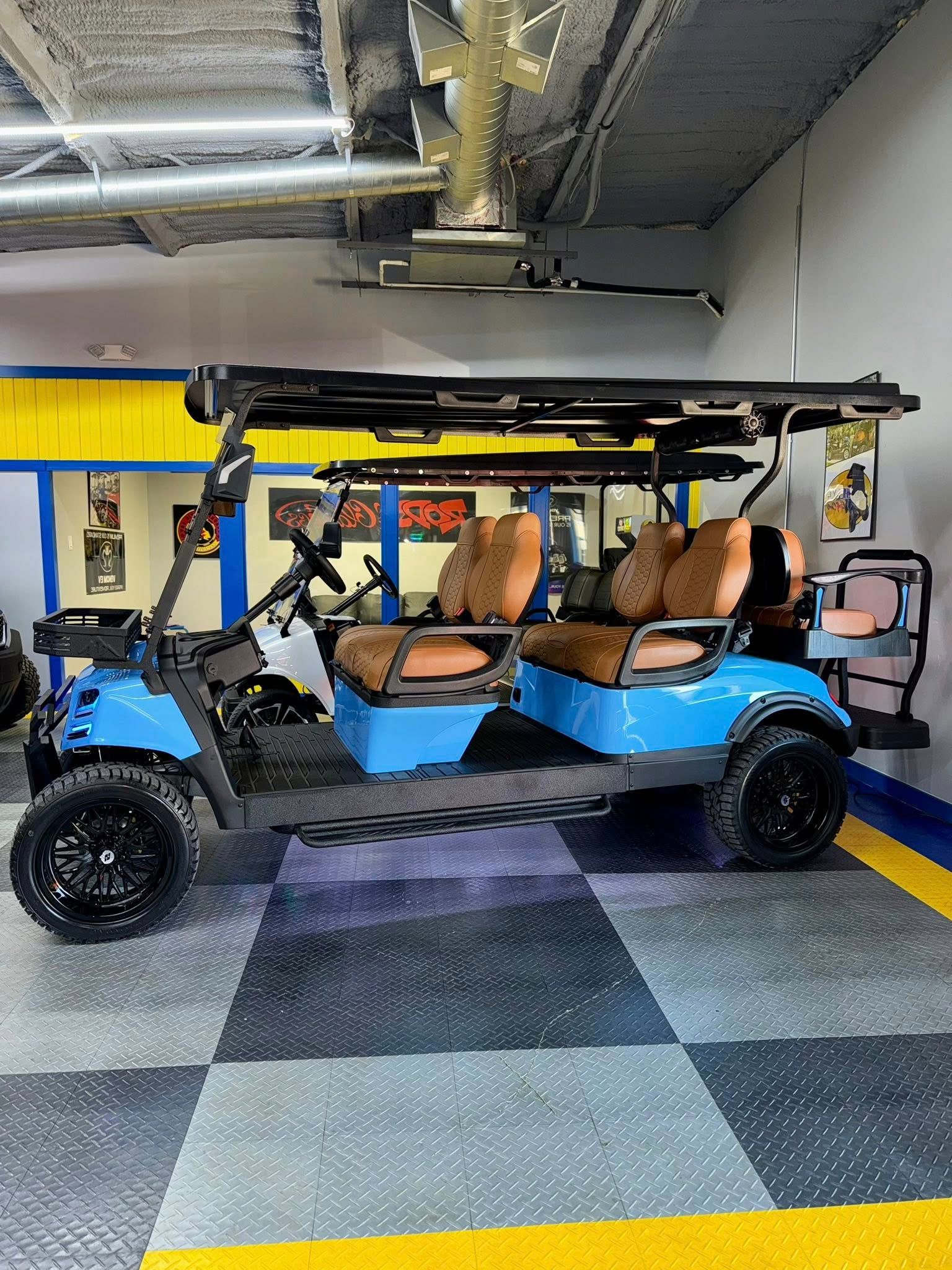 Blue golf cart with brown seats, black wheels, and a canopy, parked indoors on a tiled floor.