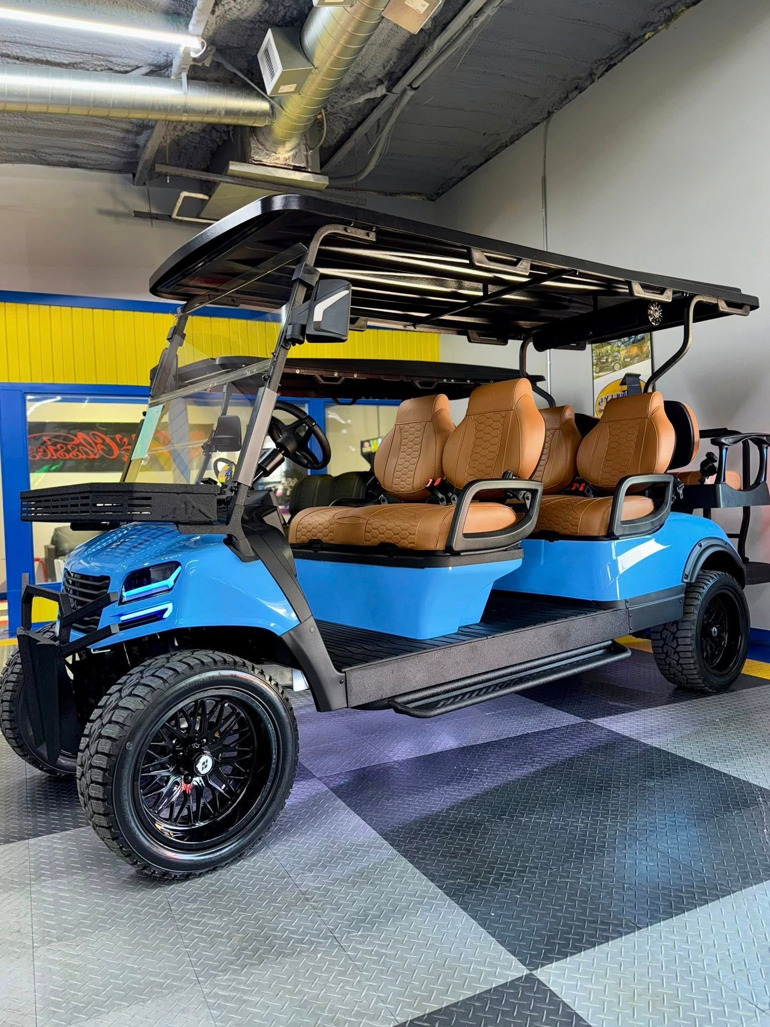 Blue golf cart with brown seats, black wheels, and roof, parked indoors.