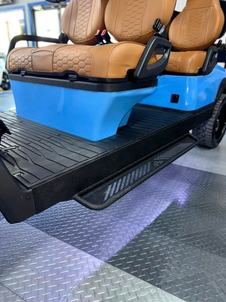 Blue golf cart with tan seats, black running boards, on a checkered floor.