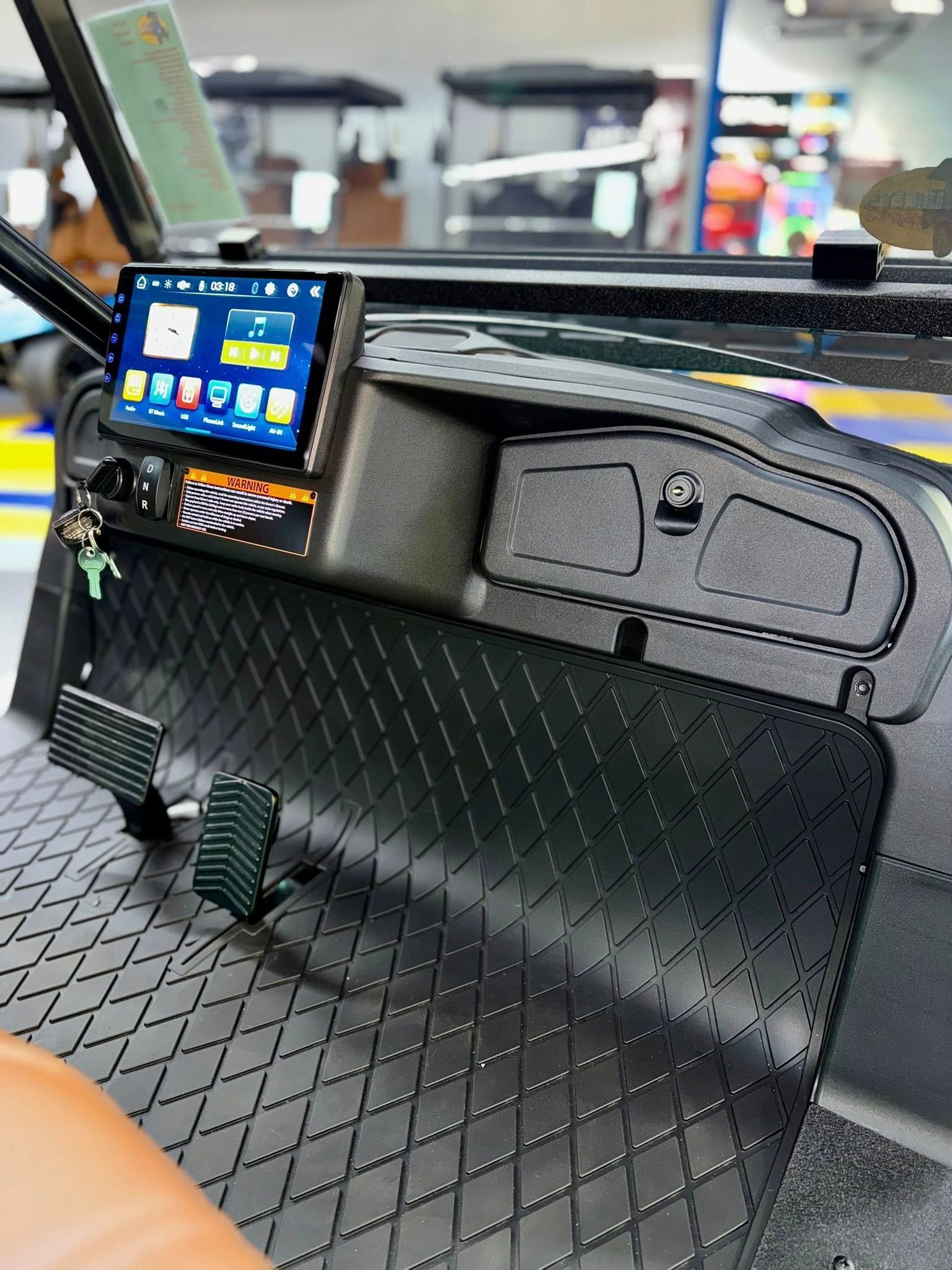 Black golf cart interior with touchscreen, pedals, and diamond-patterned floor.
