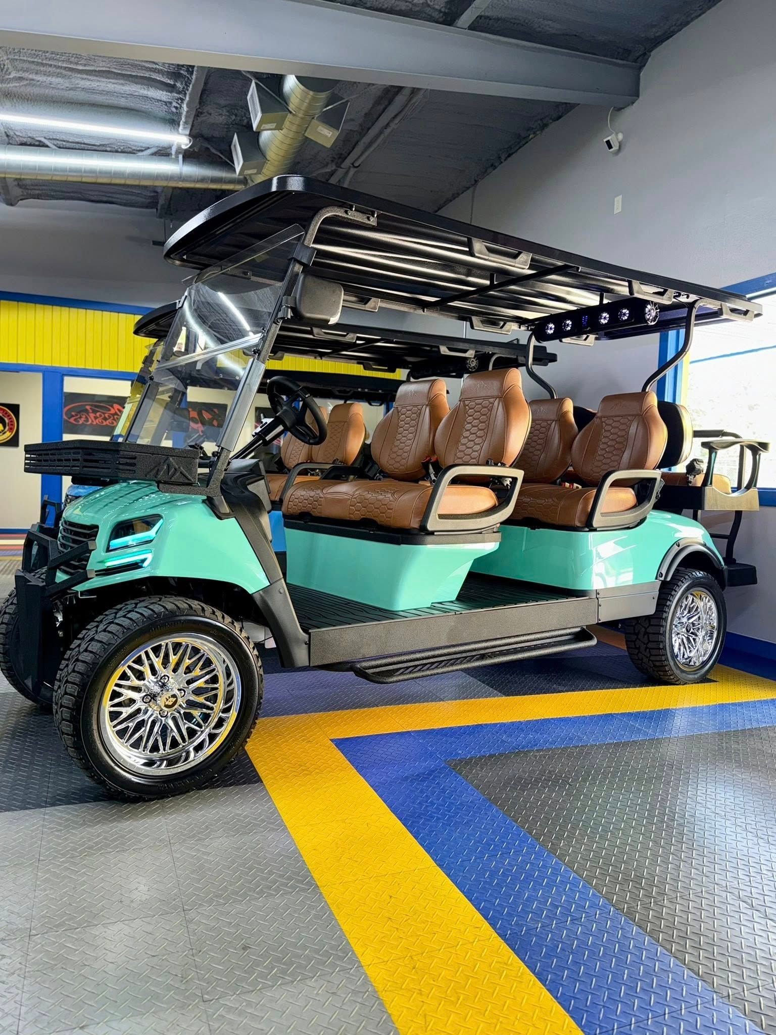 Teal golf cart with custom brown seating, black roof, and chrome rims, parked indoors on a blue and yellow surface.