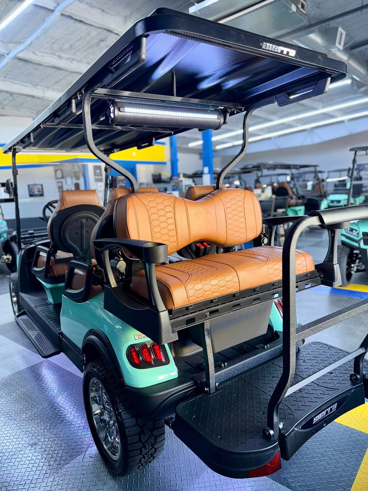 Teal golf cart with brown seats, black roof and accessories, parked indoors.