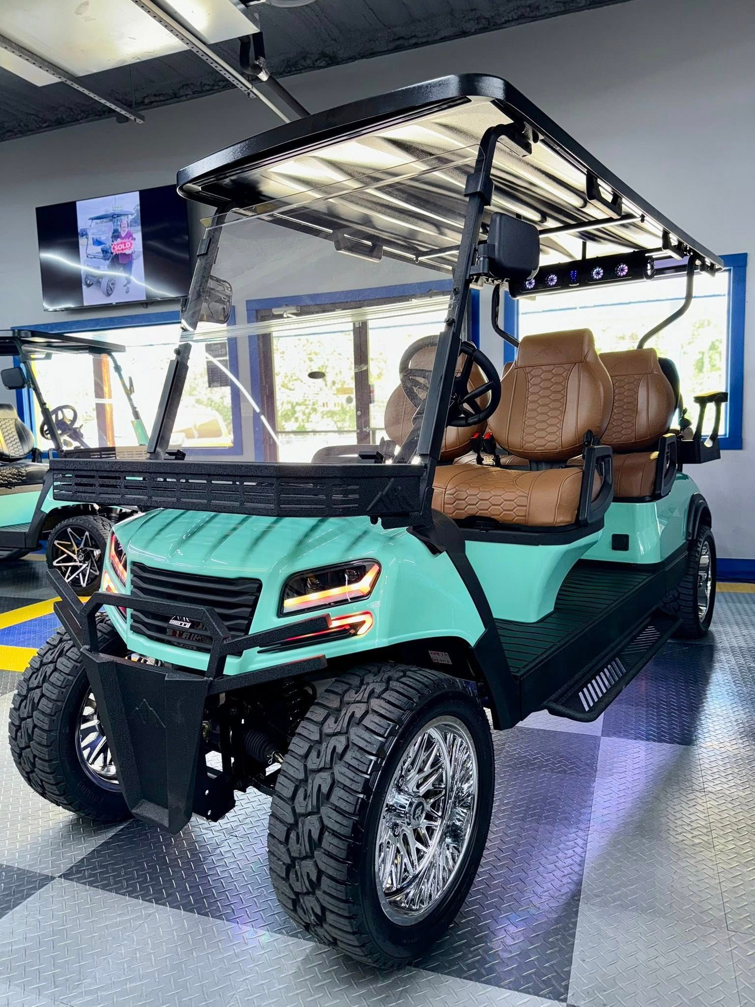 Turquoise custom golf cart with brown leather seats, chrome wheels, and off-road tires, indoors.