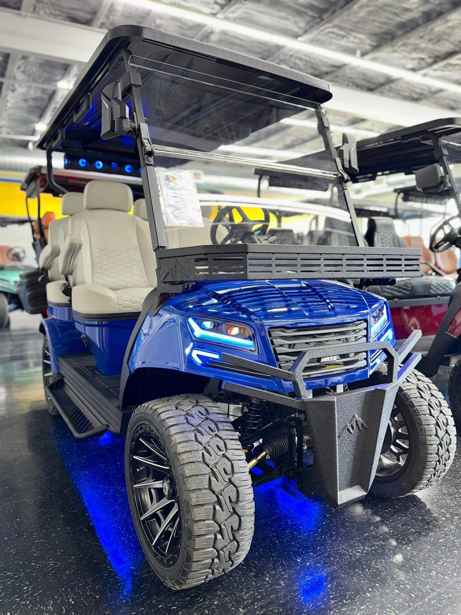 Blue custom golf cart with off-road tires, underglow, and a black roof, parked indoors.