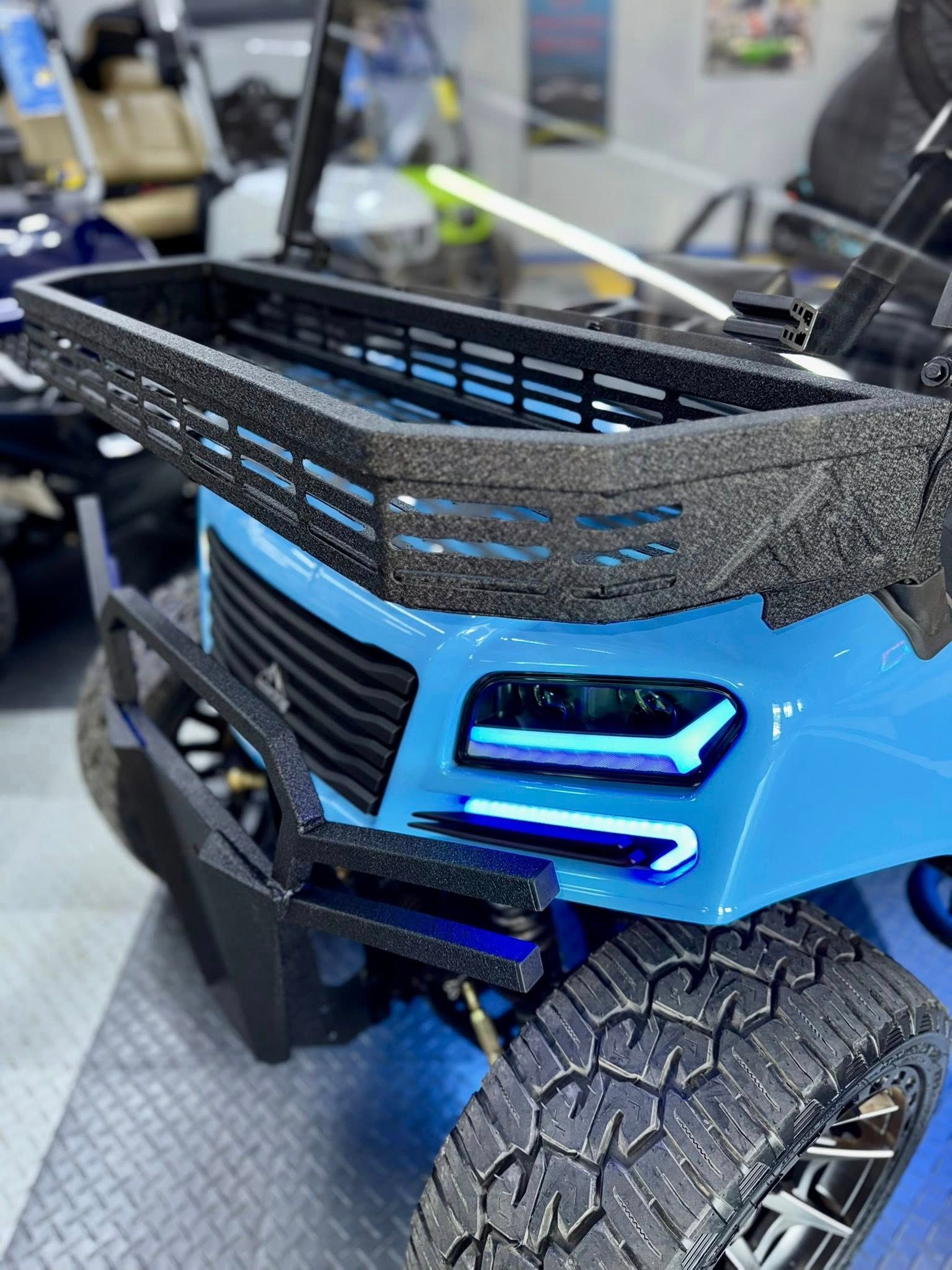 Blue custom golf cart with off-road tires and LED lights.