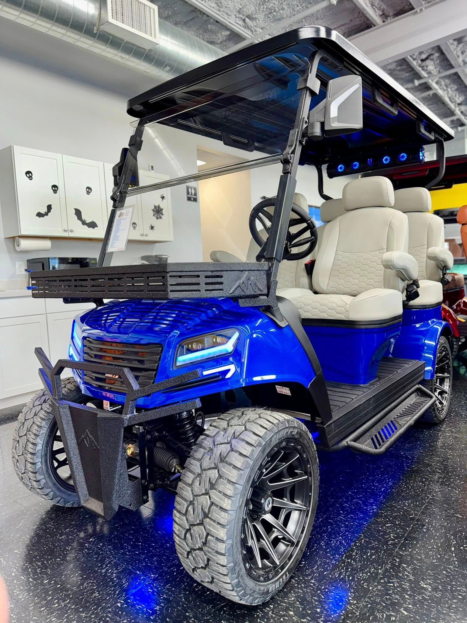 Blue customized golf cart with black accents, oversized tires, and beige seats indoors.