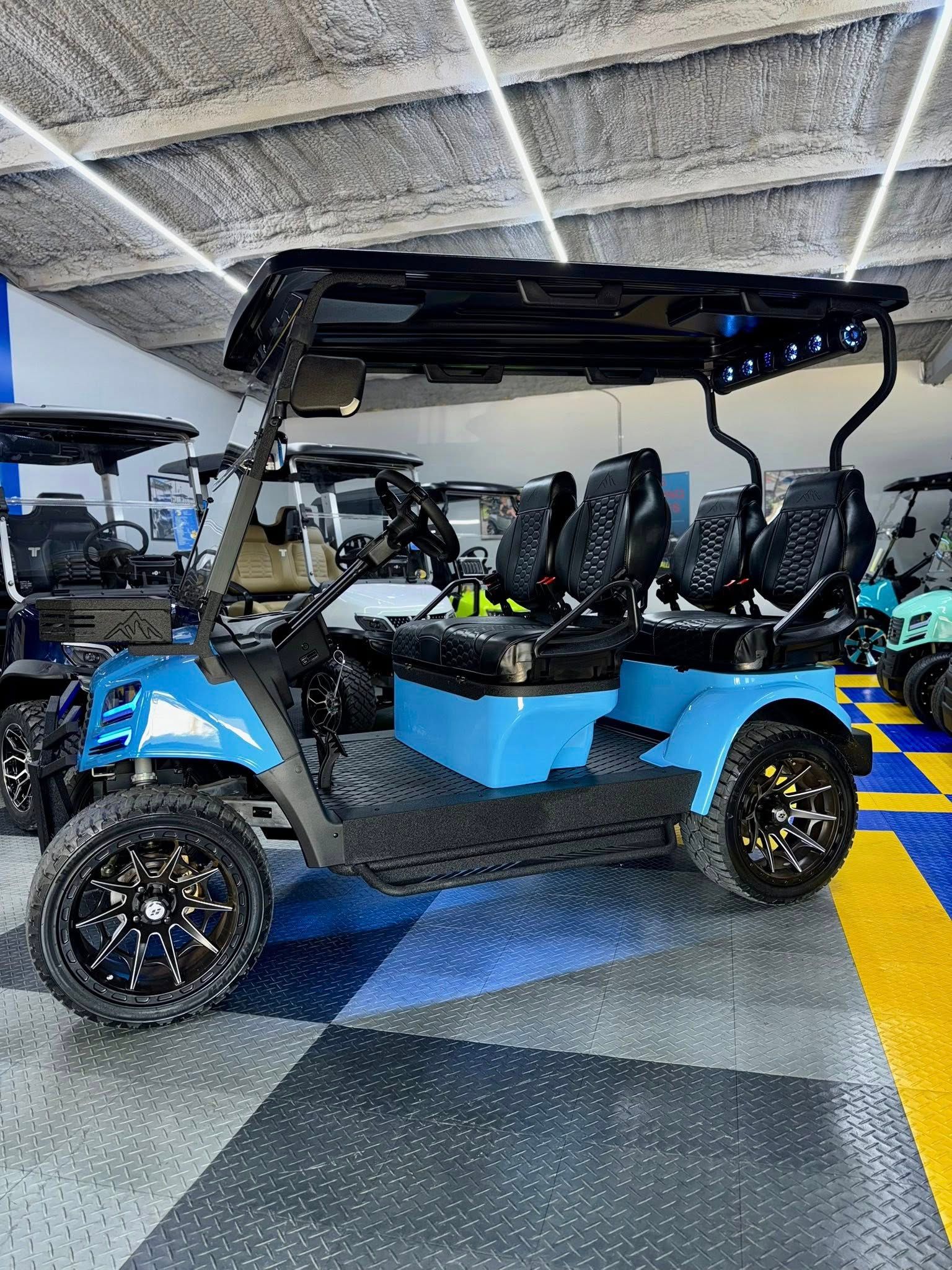 Blue and black six-person golf cart with black wheels and canopy, parked indoors on a checkered floor.