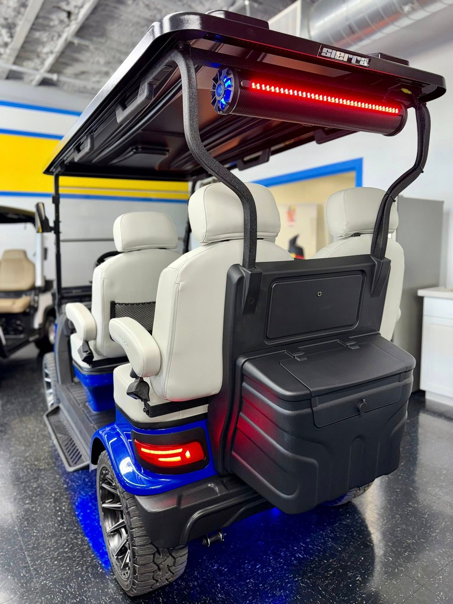 Blue golf cart with four white seats, black roll bar, red light bar, and storage box.