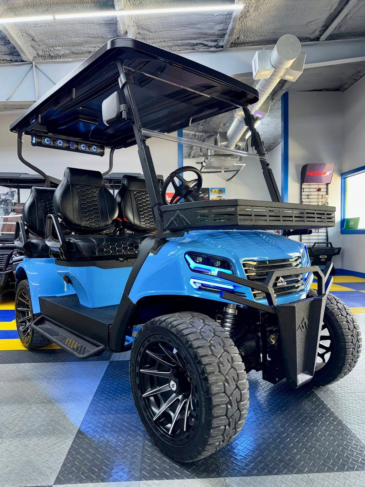Blue golf cart with black accents and off-road wheels, parked indoors.