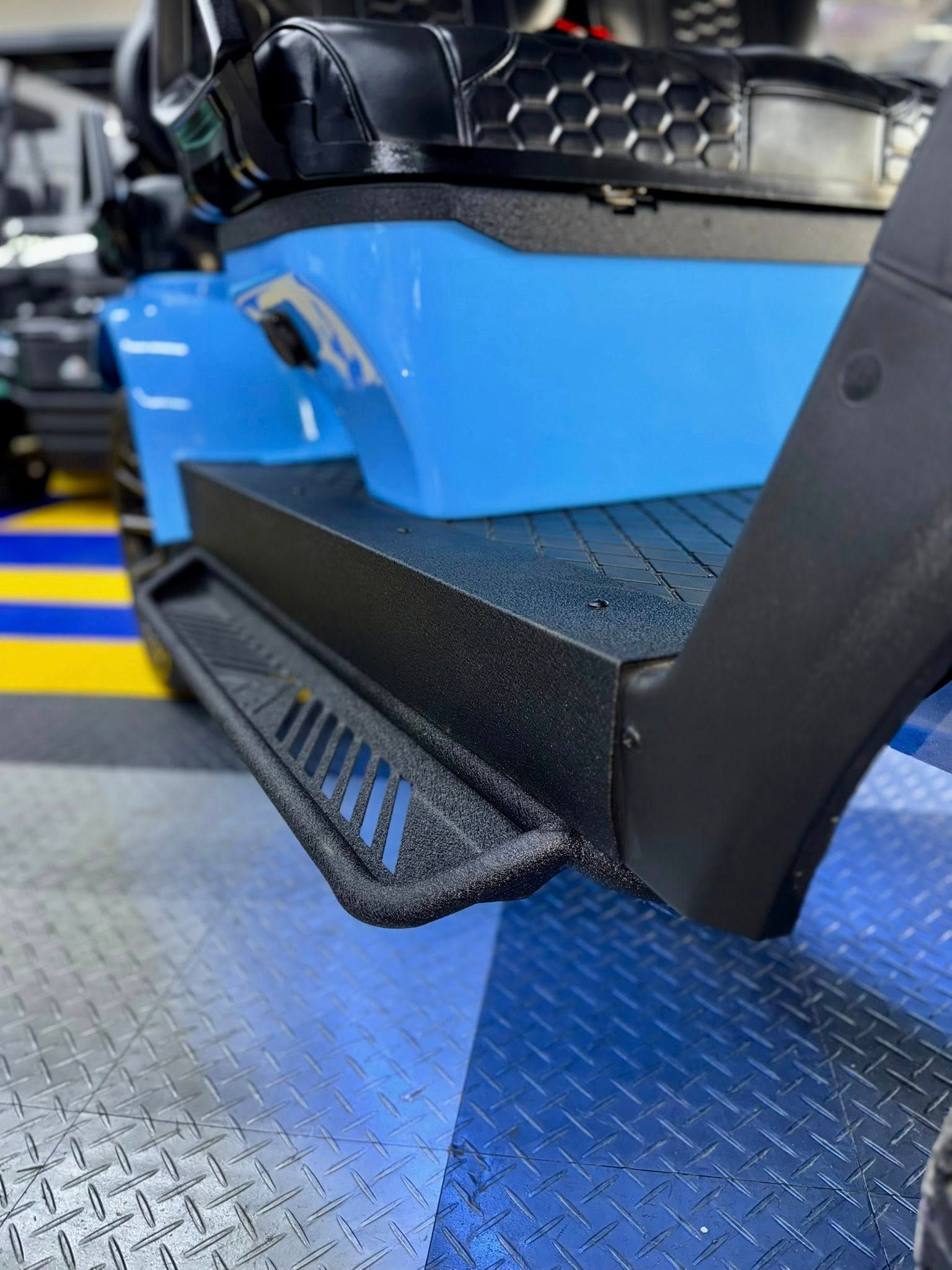 Light blue vehicle step with black, textured trim and a side step on a blue surface.